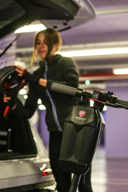 Kobieta w czerni obok skutera i otwartego bagażnika w garażu.