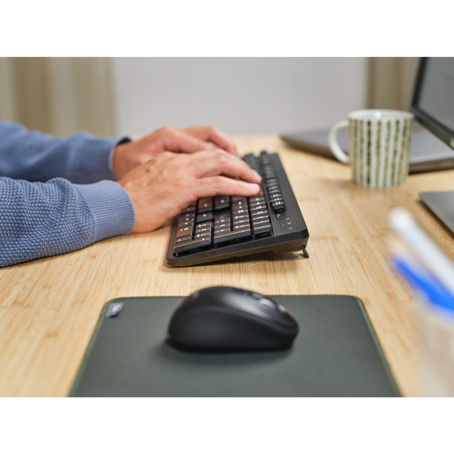 Una persona sta digitando su una tastiera nera con un mouse e un tappetino per il mouse visibili.