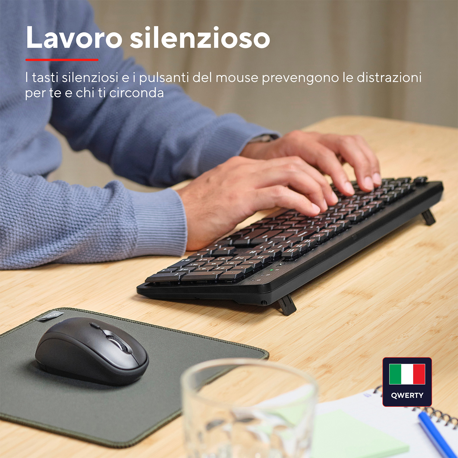Mani che digitano su una tastiera, un mouse e un tappetino su un tavolo di legno.