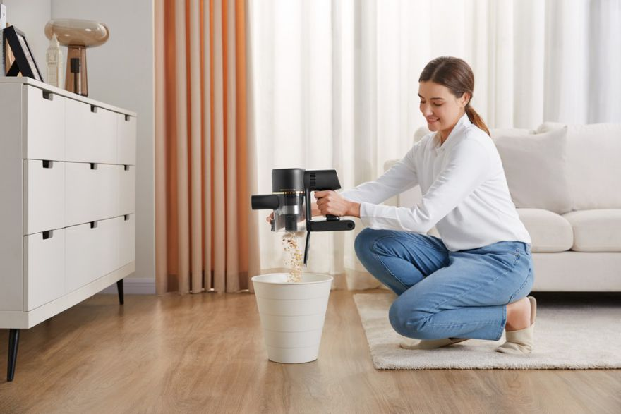 Femme vidant un aspirateur dans une poubelle. Tapis de couleur claire.