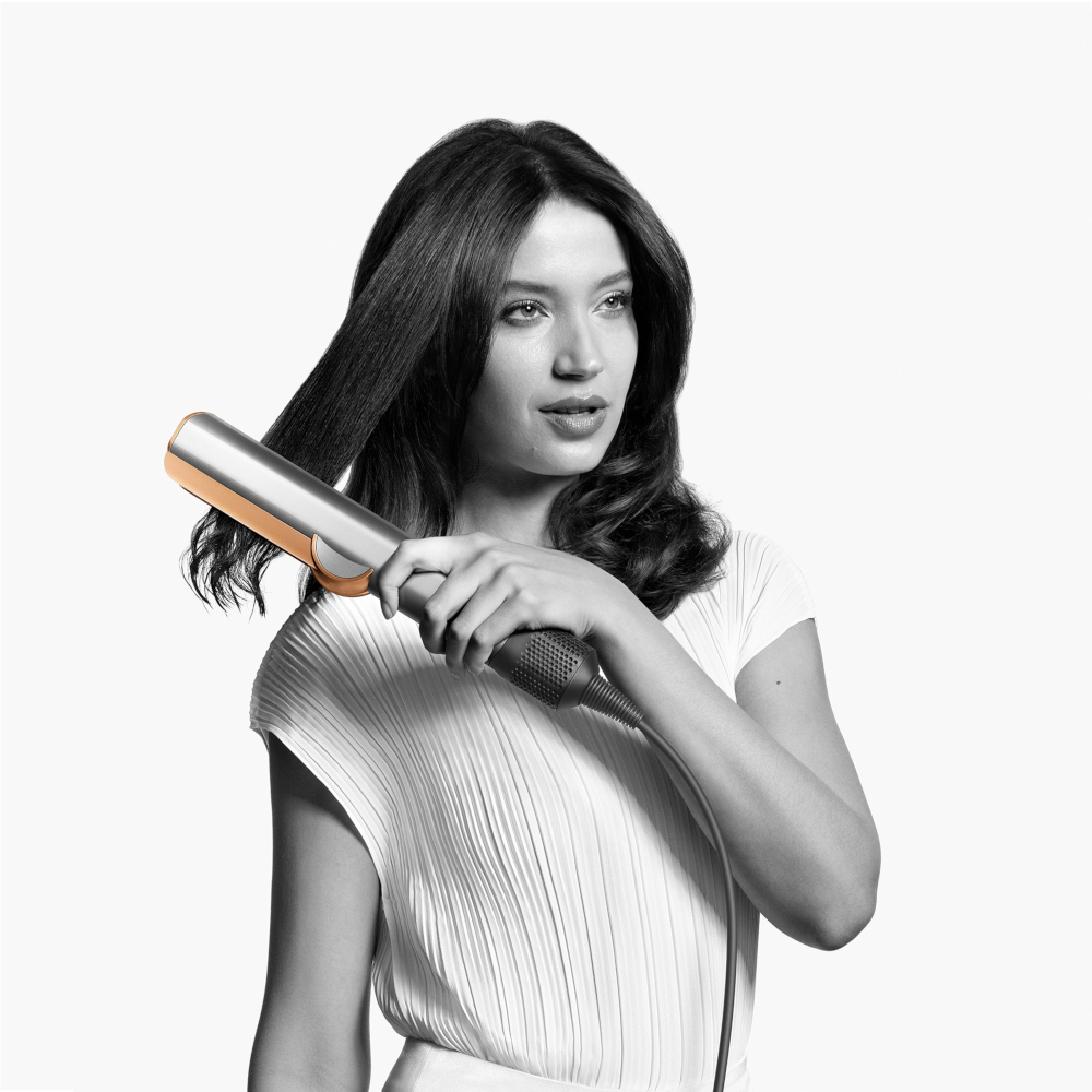 Woman using a hair straightener. She holds it with her right hand.