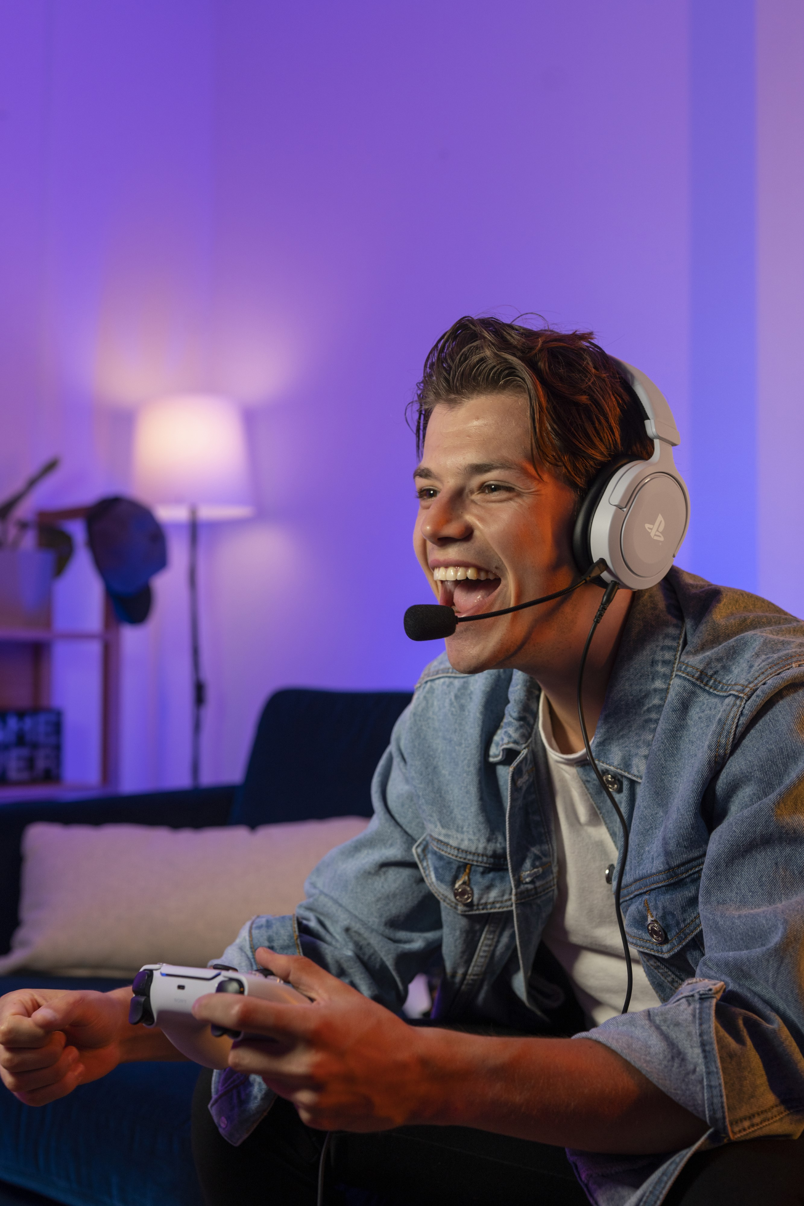 Man wearing headset and denim jacket, smiling while playing a video game.
