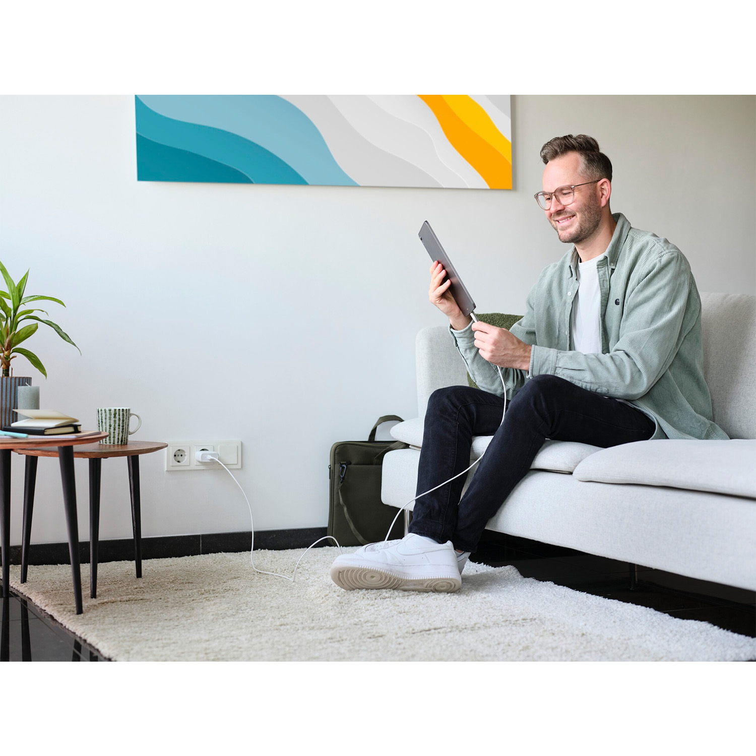 Uomo su un divano che usa un tablet, con una lampada e un tavolino.