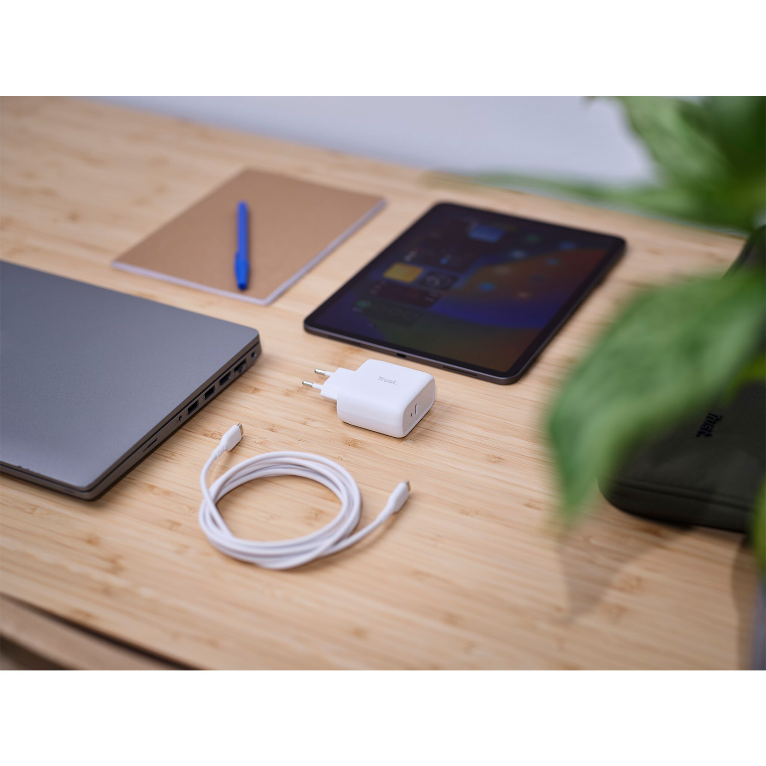Laptop, tablet, taccuino e caricabatterie su un tavolo di legno.