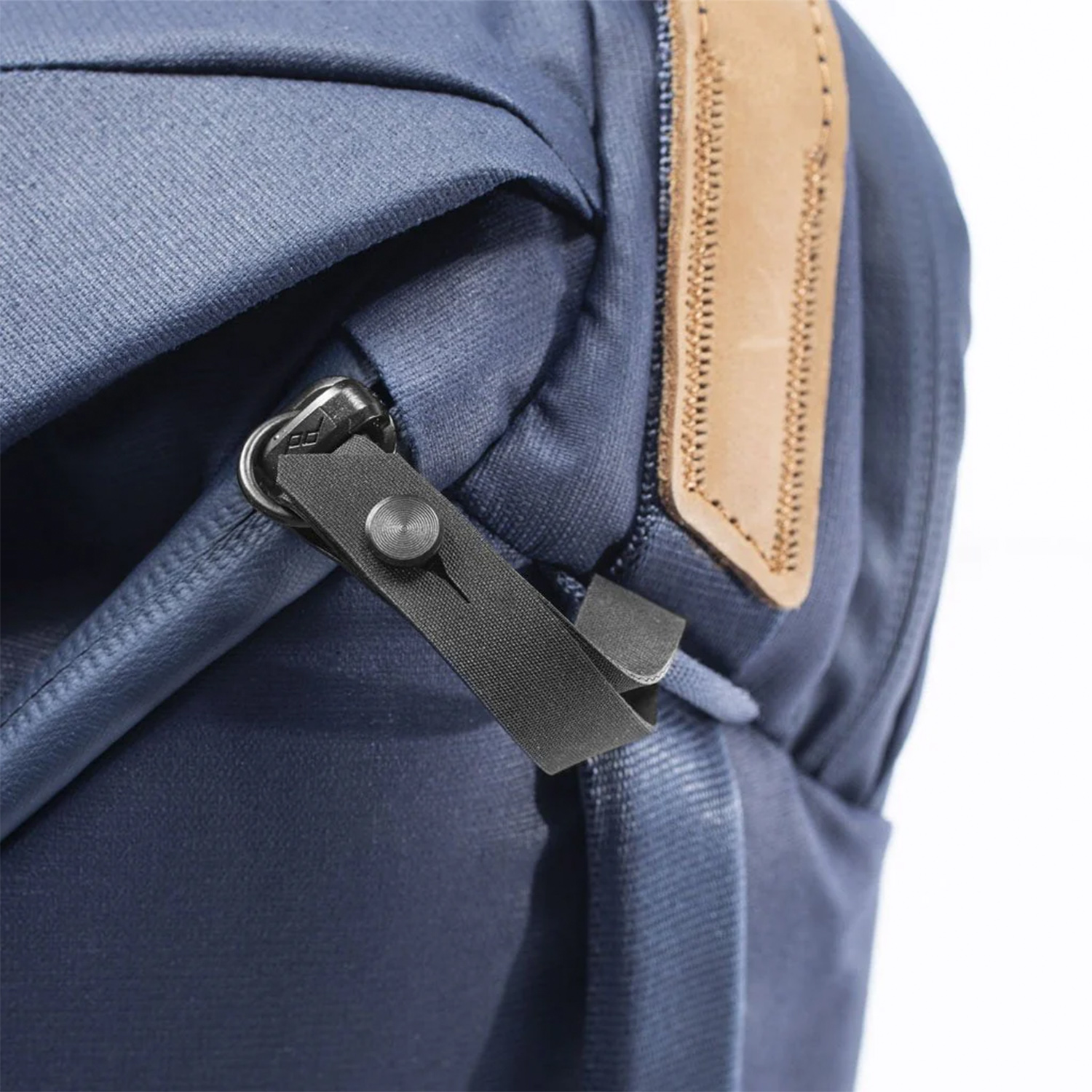 Primo piano della cerniera di uno zaino blu navy. Toppa in pelle marrone visibile.
