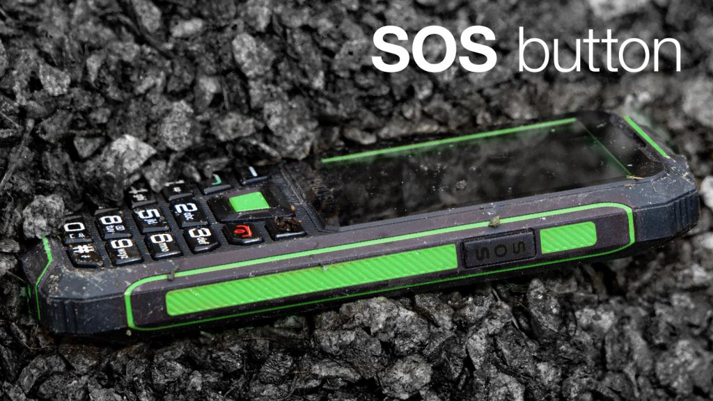 Robusztus telefon aszfalton. SOS gomb címkével. Sötét, zöld ékezetekkel.
