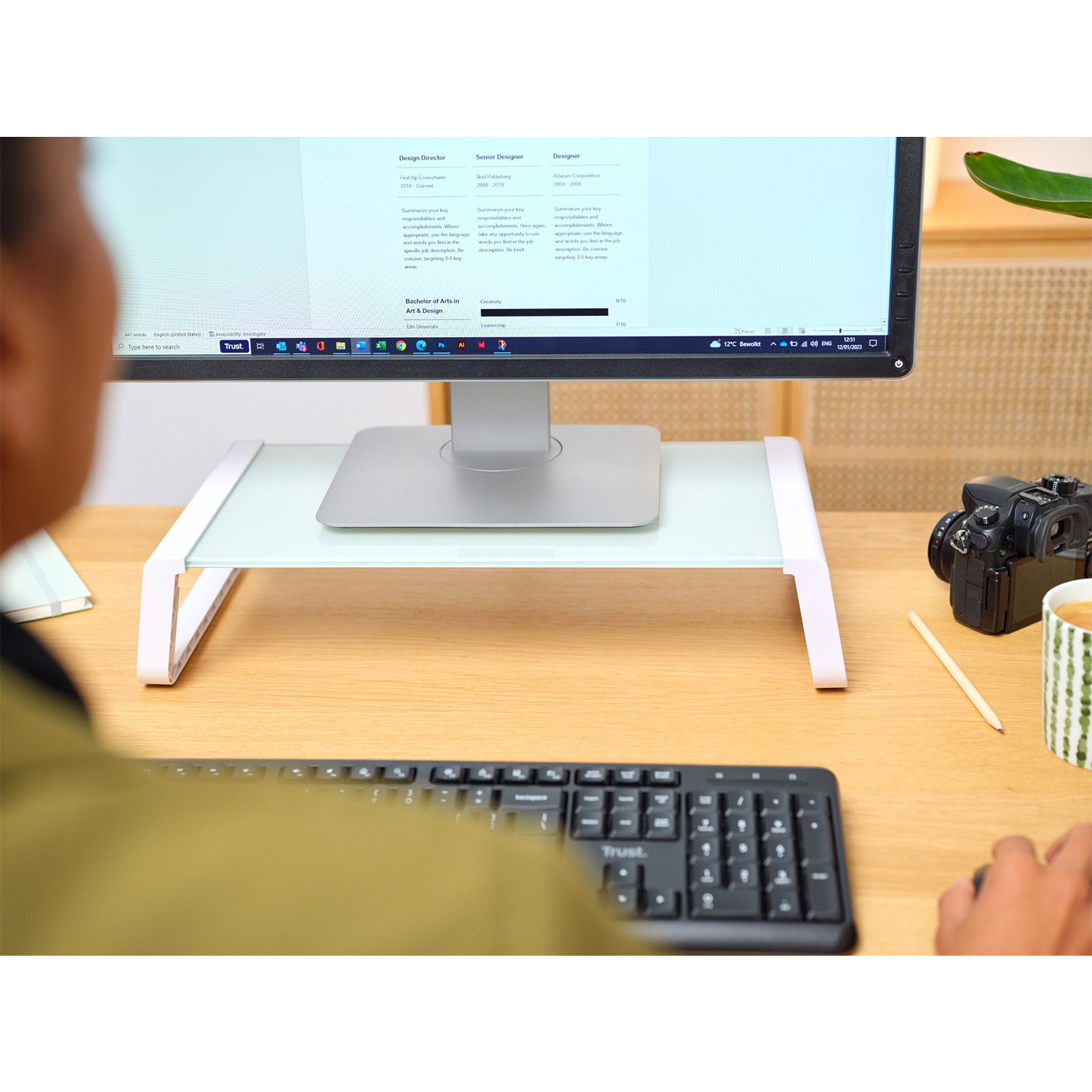 Persona che usa un computer con monitor su supporto, tastiera e fotocamera sulla scrivania.