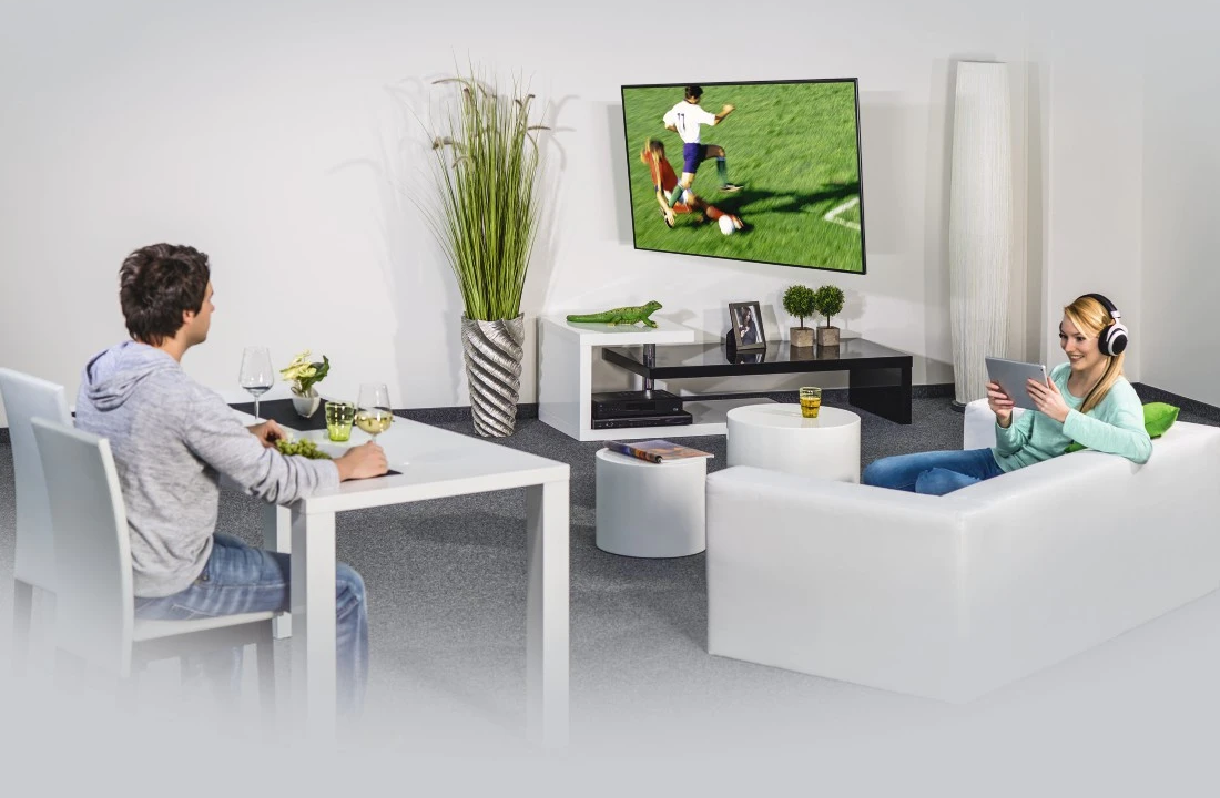 Nappali TV-vel, egy párral és fehér bútorokkal. A világítás lágy.