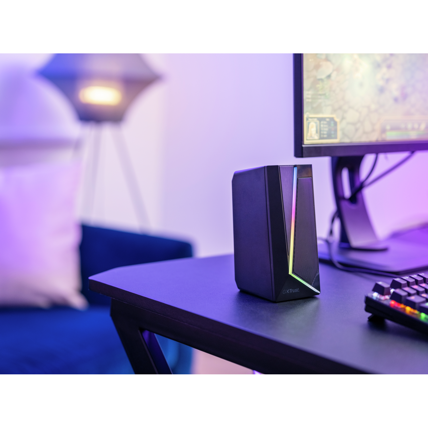 Black speaker with colorful lights on a desk. Computer monitor visible in the background.
