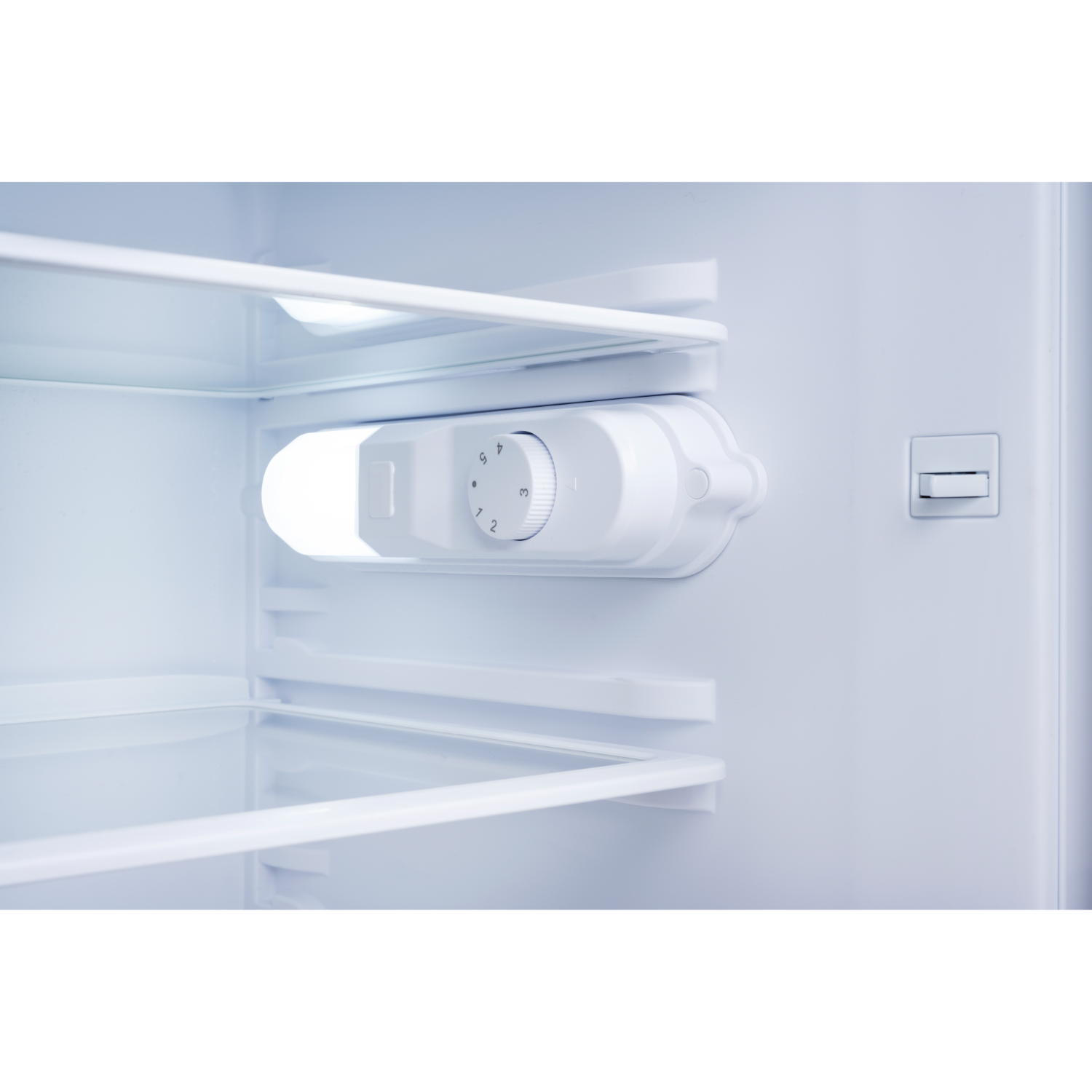 Close-up of a refrigerator interior. White shelves and a control dial. Empty. The view is from inside.