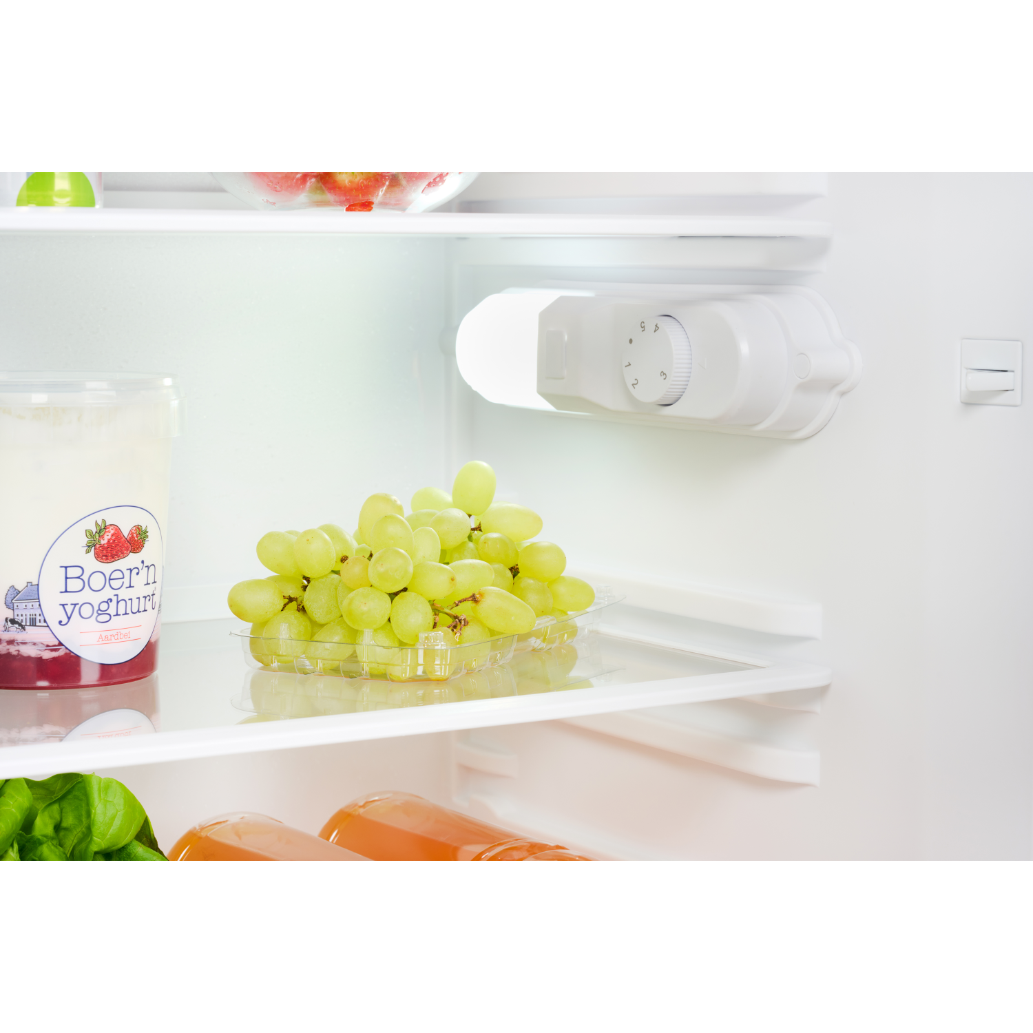 Inside a fridge: grapes in a container, yogurt, and a control panel. White interior.