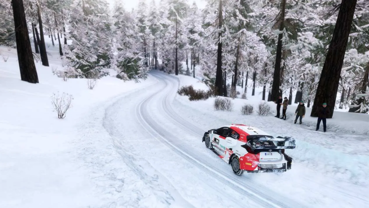 Ein Rallye-Auto auf einer schneebedeckten Straße in einem Wald mit Bäumen und Zuschauern.