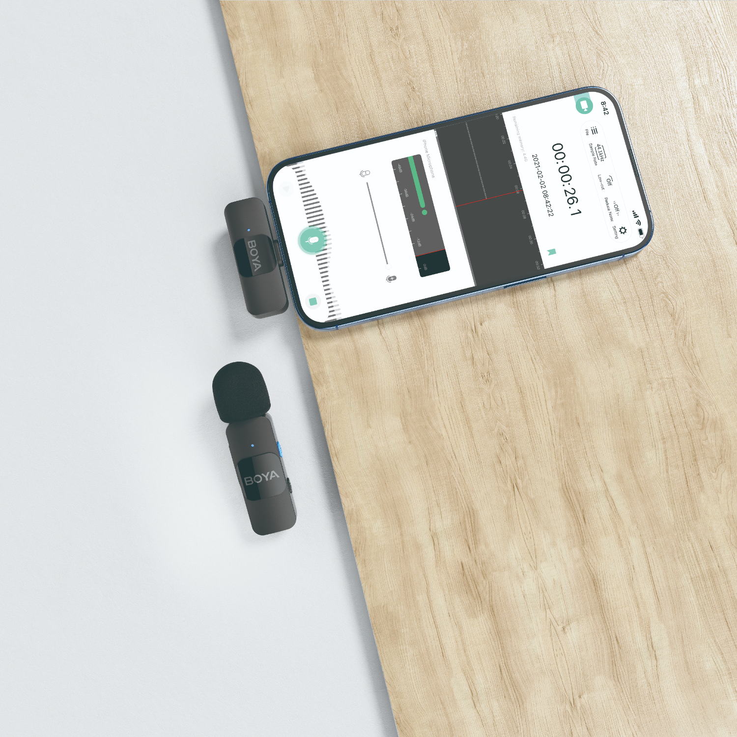 Een zwarte microfoon ligt naast een telefoon op een houten oppervlak. De telefoon toont een opname-interface.