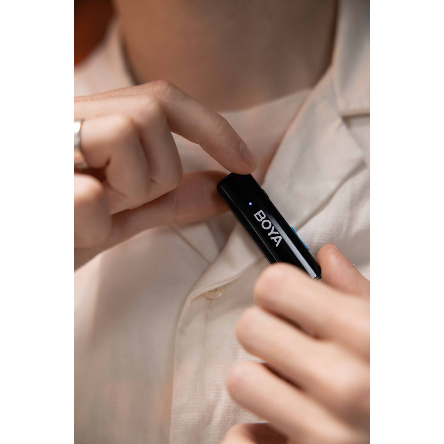 Persoon die een zwarte BOYA draadloze microfoon aan een licht overhemd vastmaakt.