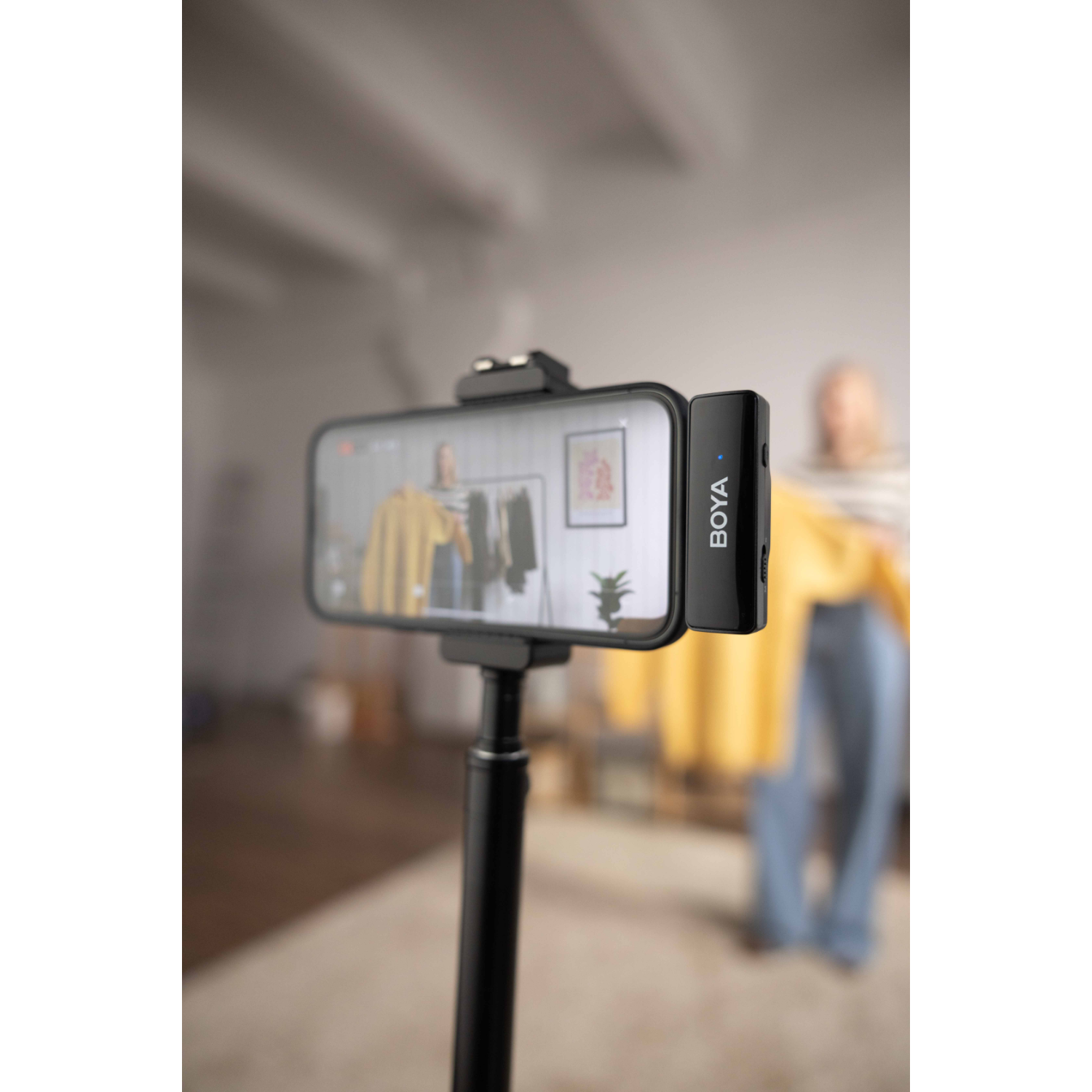 Smartphone op statief filmt een vrouw met gele trui. Een zwarte microfoon zit rechts.