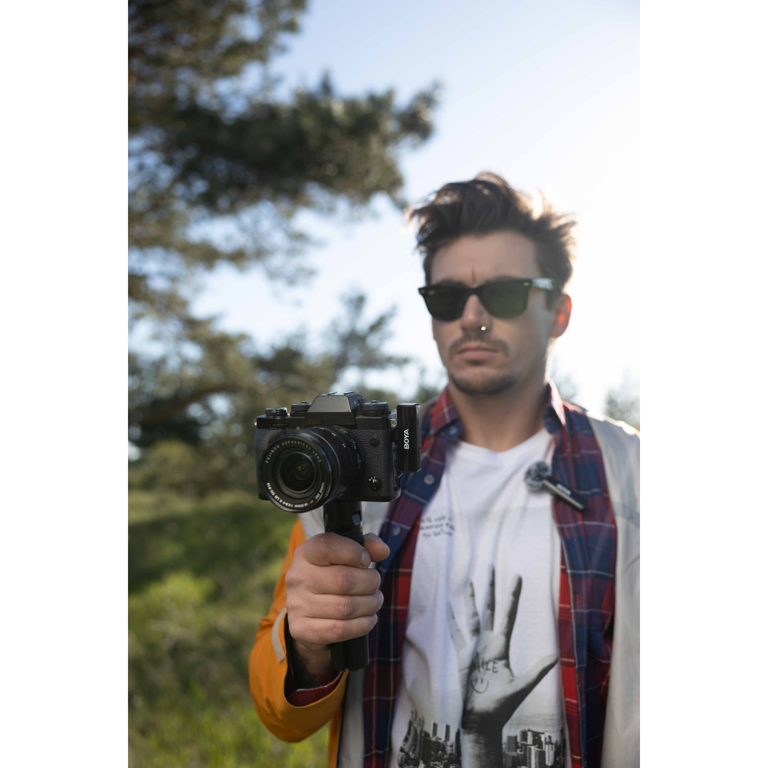 Een man met een zonnebril die een camera vasthoudt, buiten.
