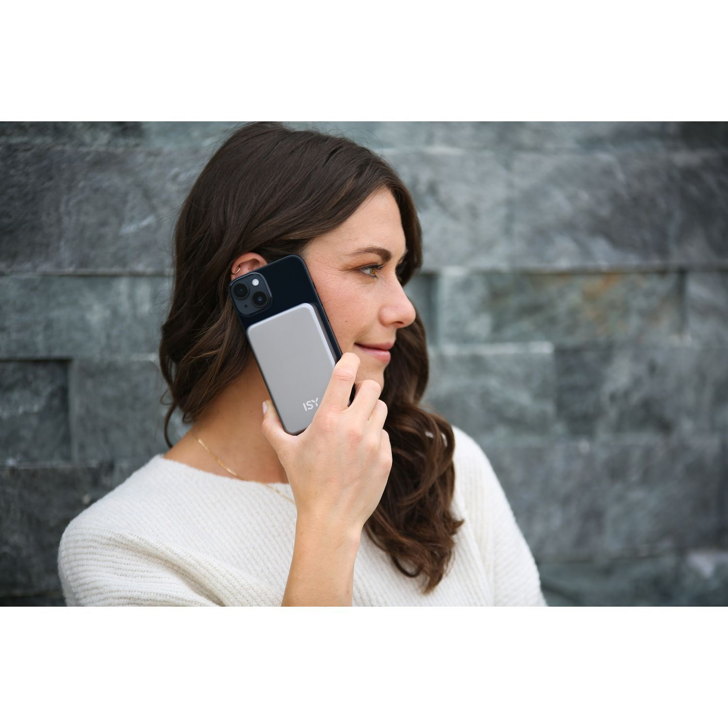 Une femme tient un téléphone à son oreille. Il y a une batterie externe argentée attachée.