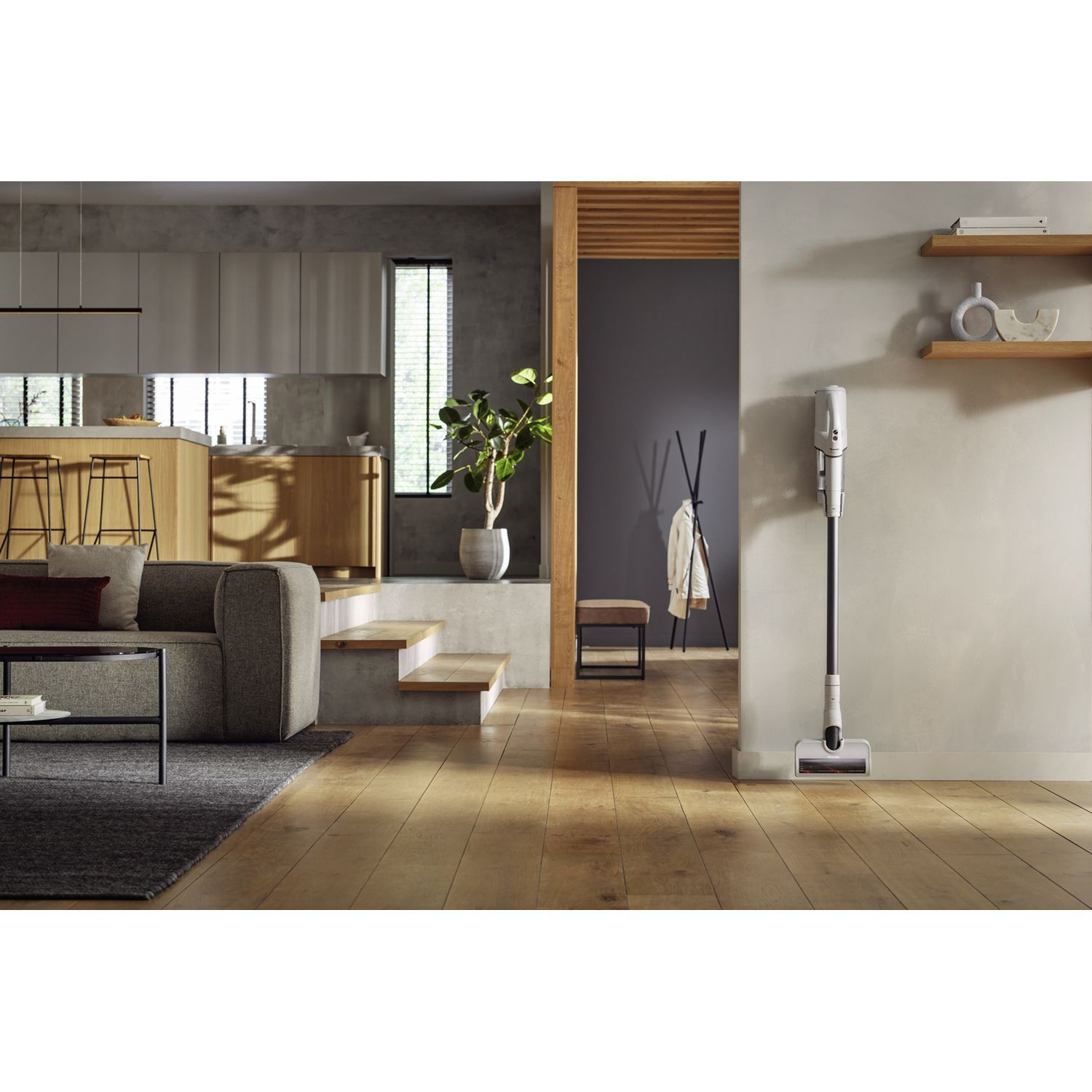 Salon moderne avec aspirateur. Sol en bois, canapé gris. Murs neutres.