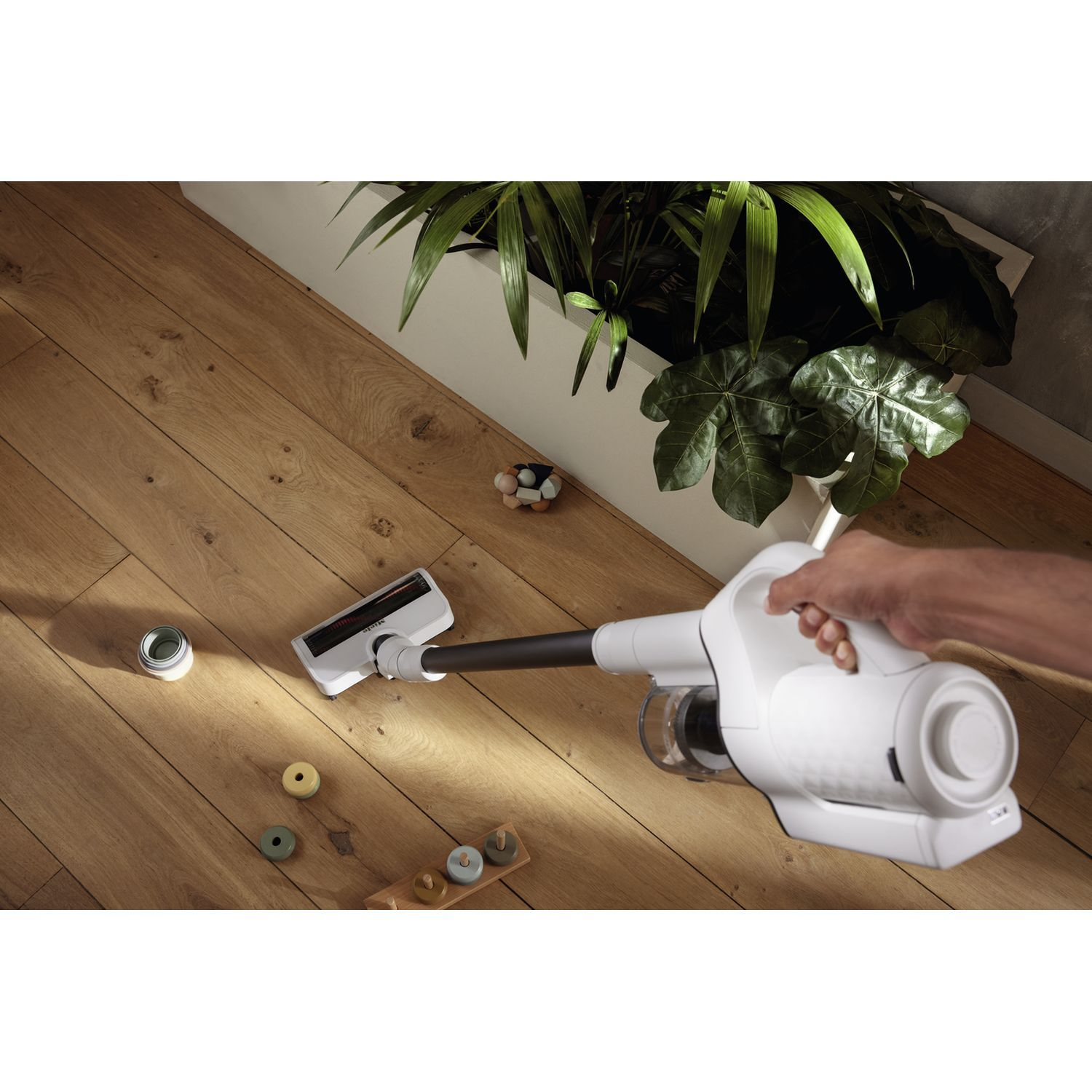 Une personne utilisant un aspirateur blanc sur un sol en bois avec quelques objets.