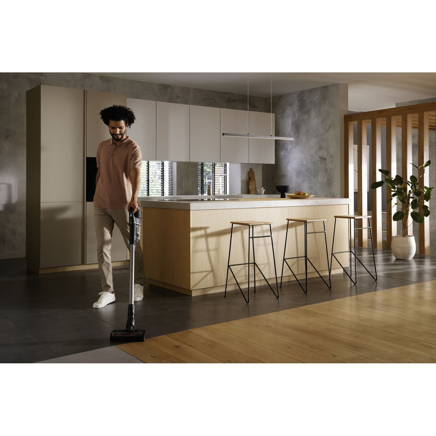 Persoon die een houten vloer stofzuigt in een moderne keuken.