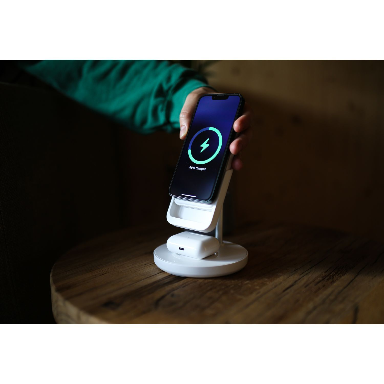 Un téléphone se charge sur un chargeur sans fil blanc, tenu par une main.