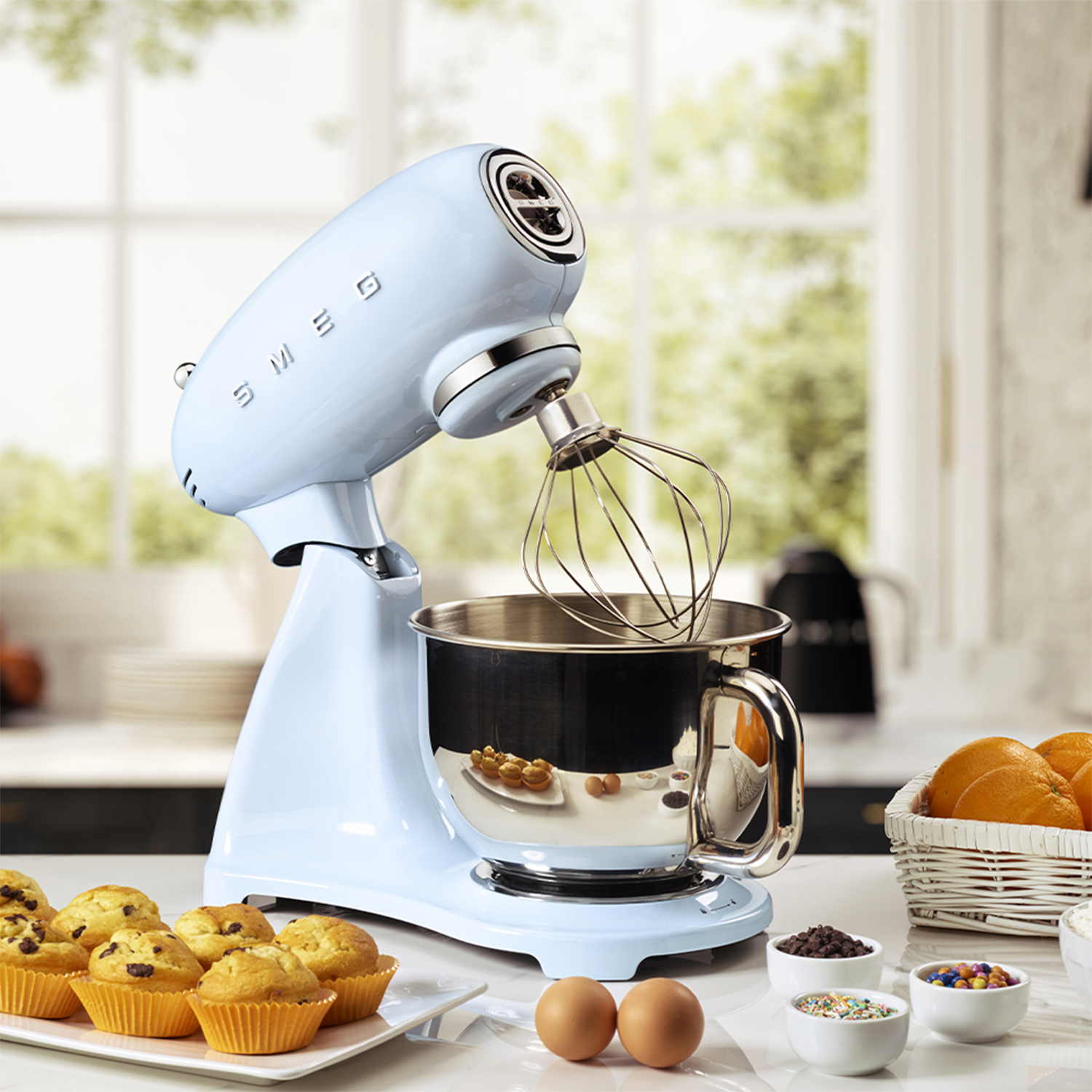 Impastatrice Smeg azzurra in un ambiente cucina con muffin, uova e ingredienti.