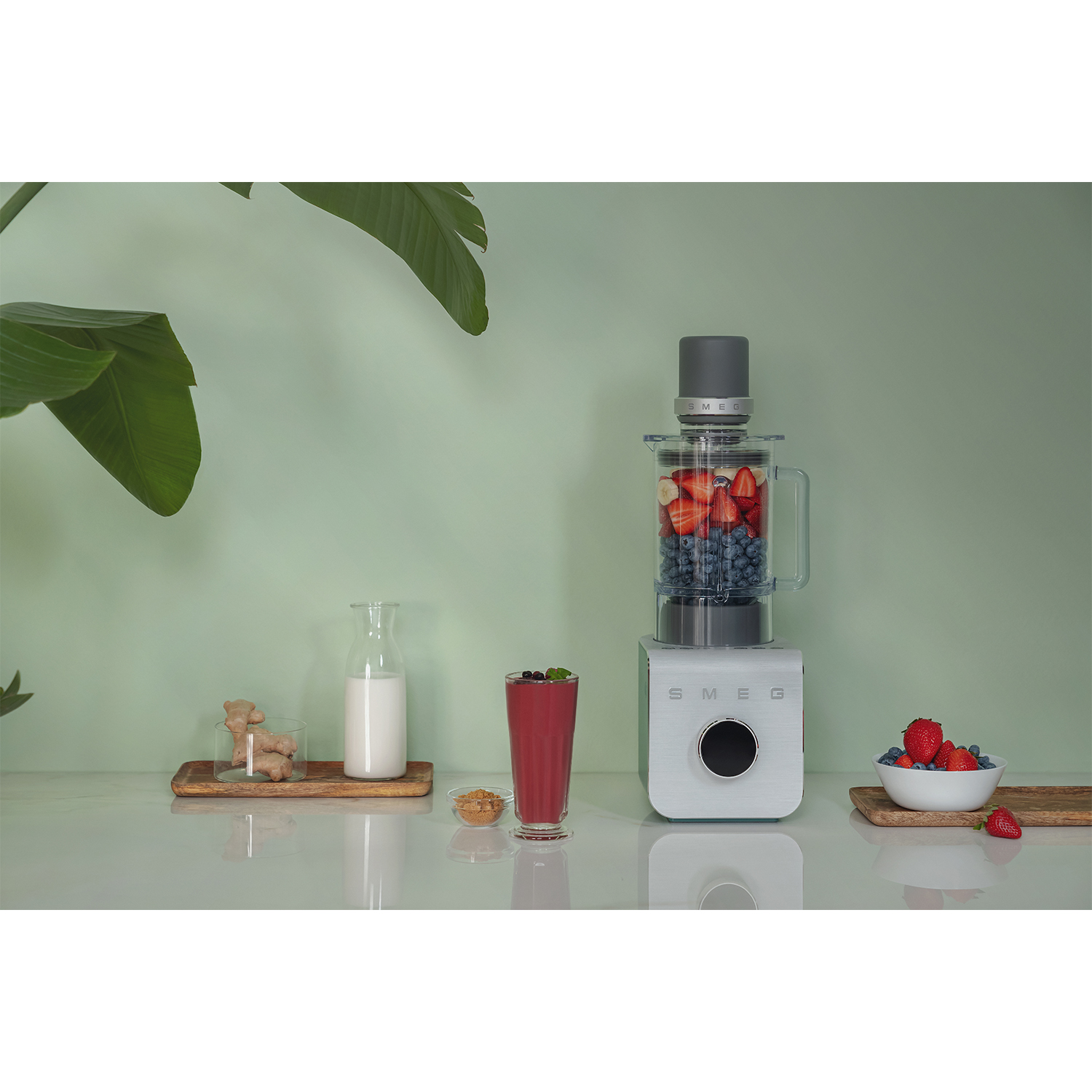 Scena di cucina con frullatore Smeg bianco, ingredienti e utensili su una superficie bianca.