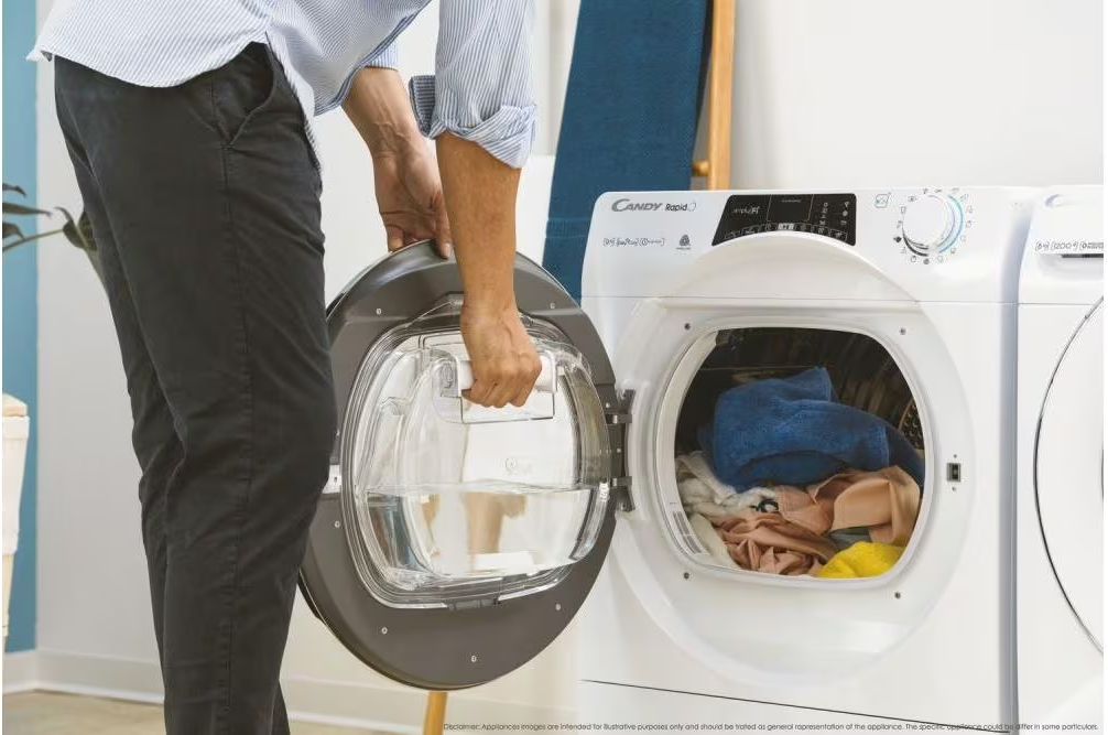 Eine Person öffnet die Tür einer Waschmaschine, die Kleidung im Inneren zeigt. Die Waschmaschine ist weiß.
