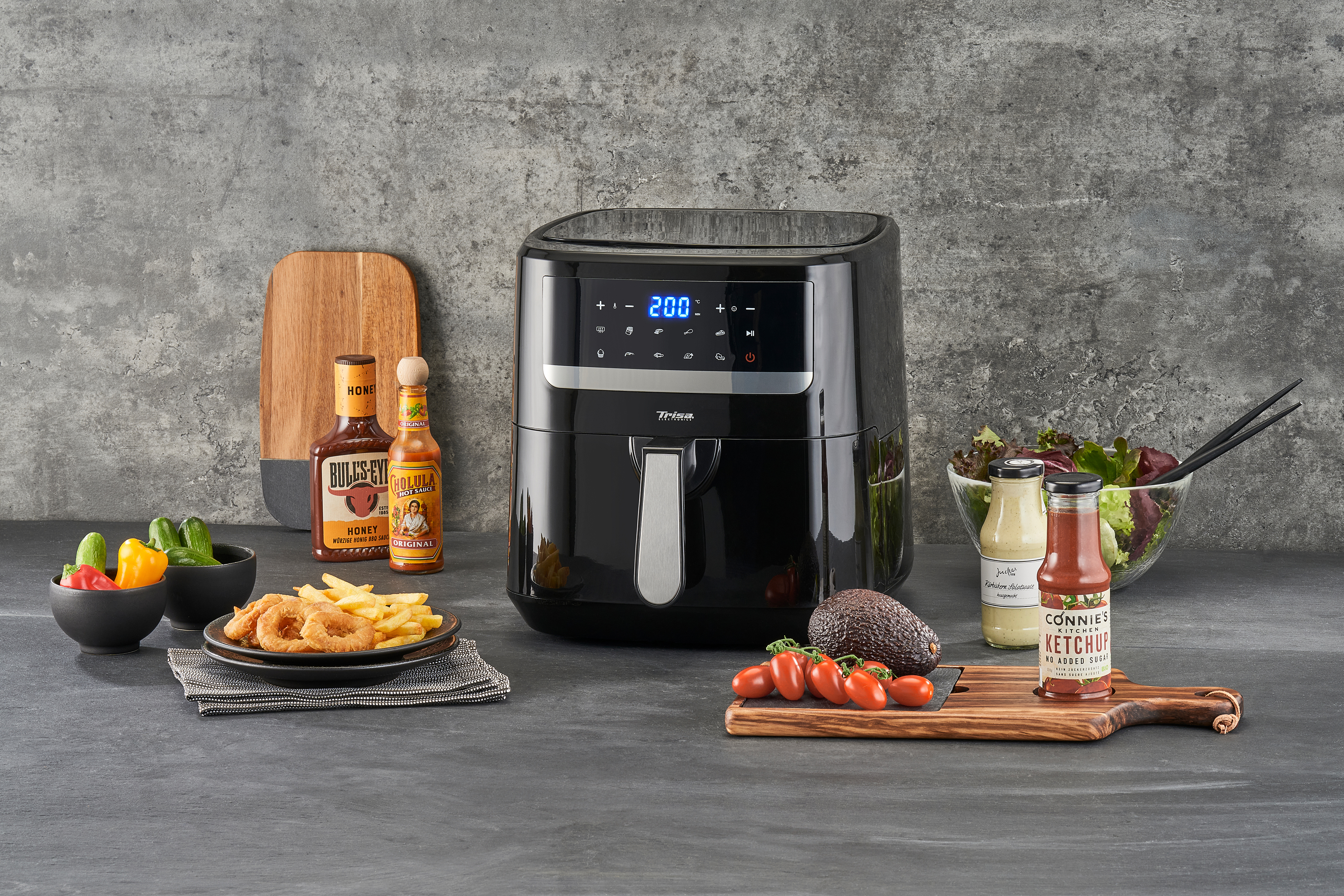 Friteuse à air noire avec nourriture sur une table, y compris sauces et légumes.