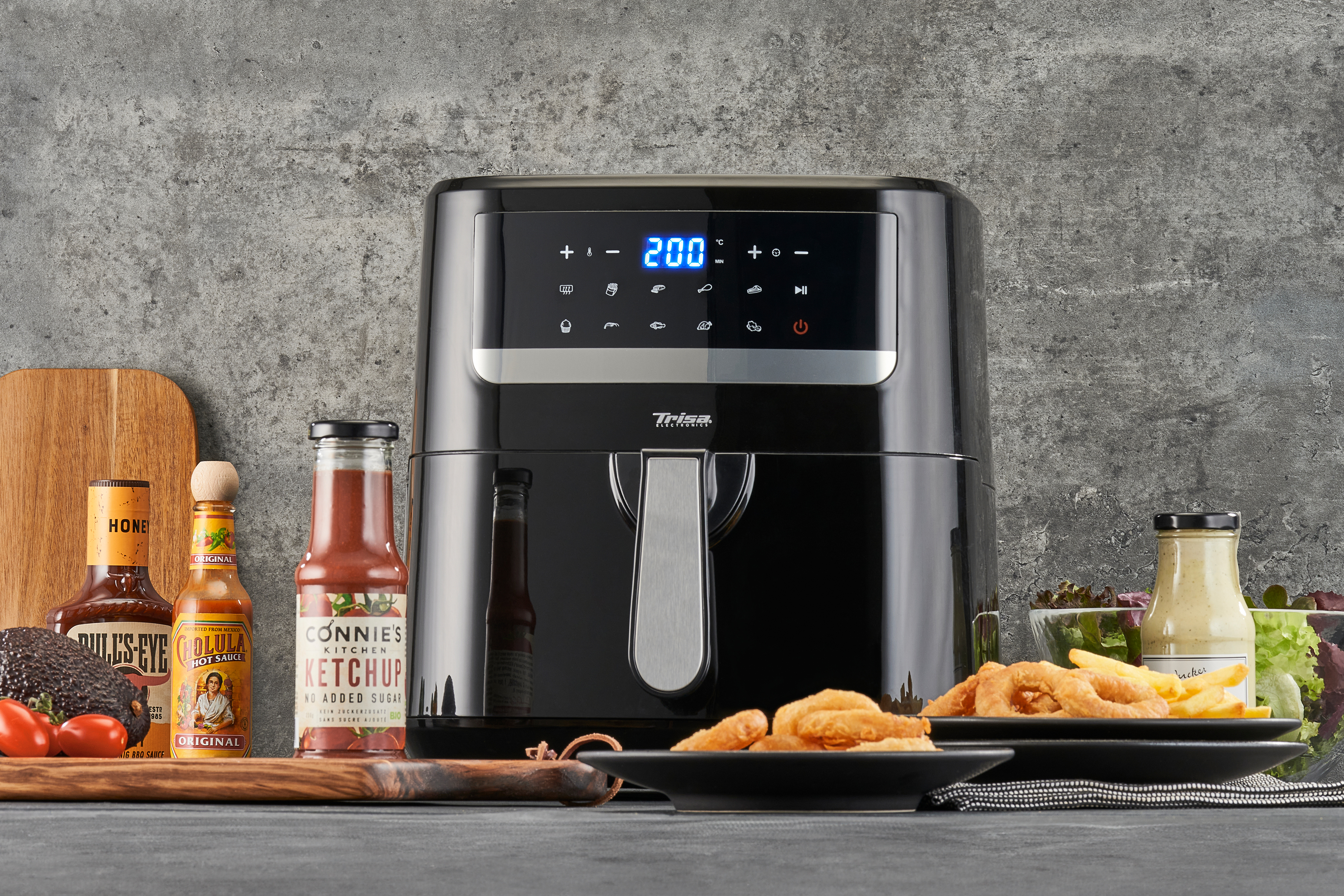 Une friteuse à air noire avec un affichage numérique, entourée de bouteilles de sauce et de nourriture.