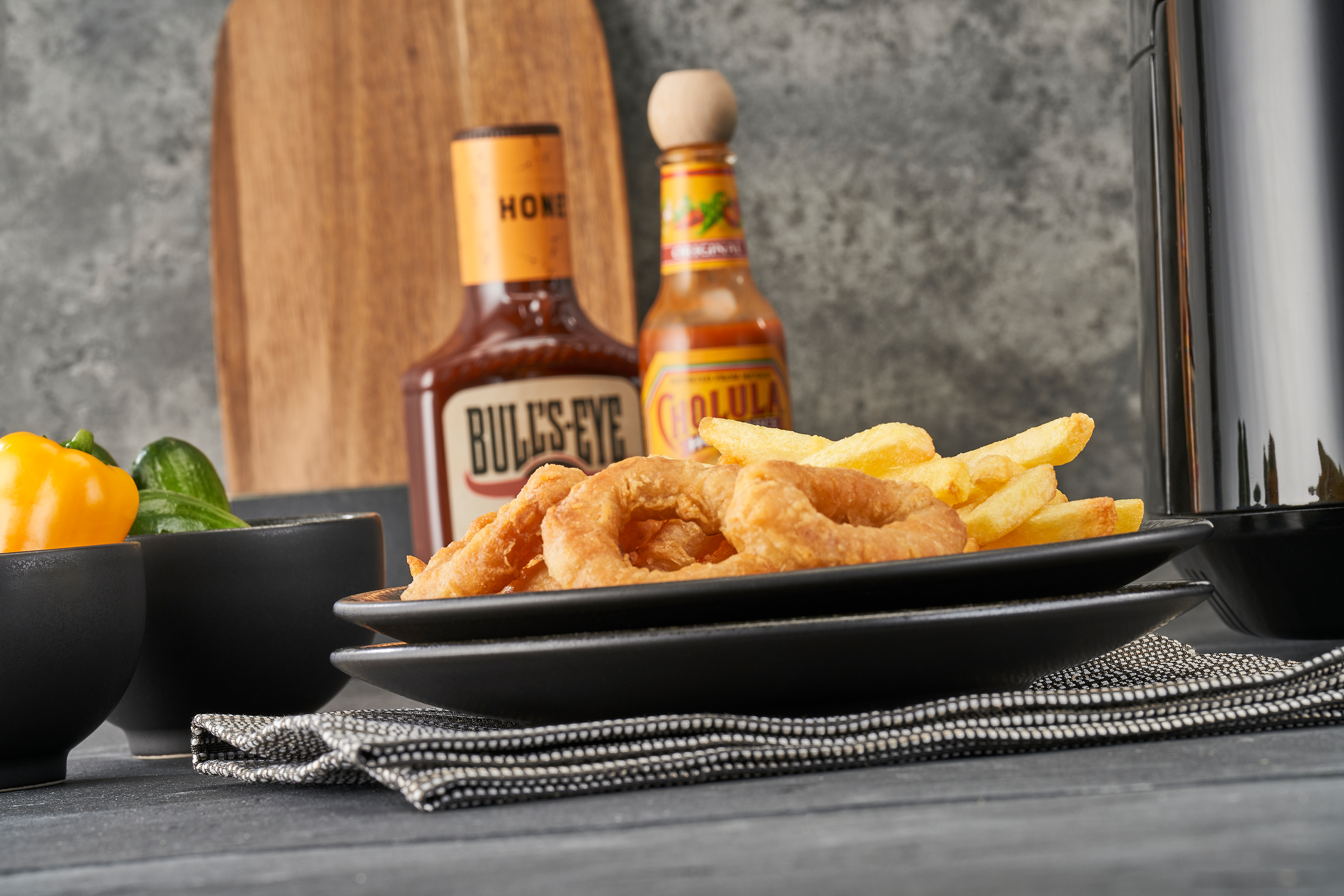 Rondelles d'oignon et frites sur une assiette avec des sauces et une planche en bois.
