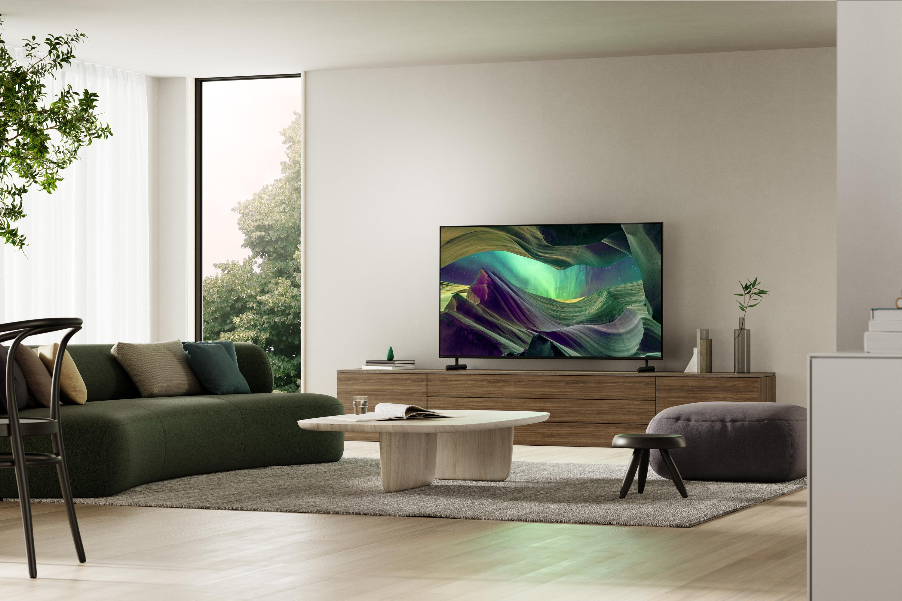 Wohnzimmer mit grünem Sofa, Fernseher, Couchtisch und großem Fenster.