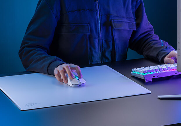 Une personne utilise une souris blanche sur un tapis de souris blanc. Un clavier avec des lumières colorées est en arrière-plan.