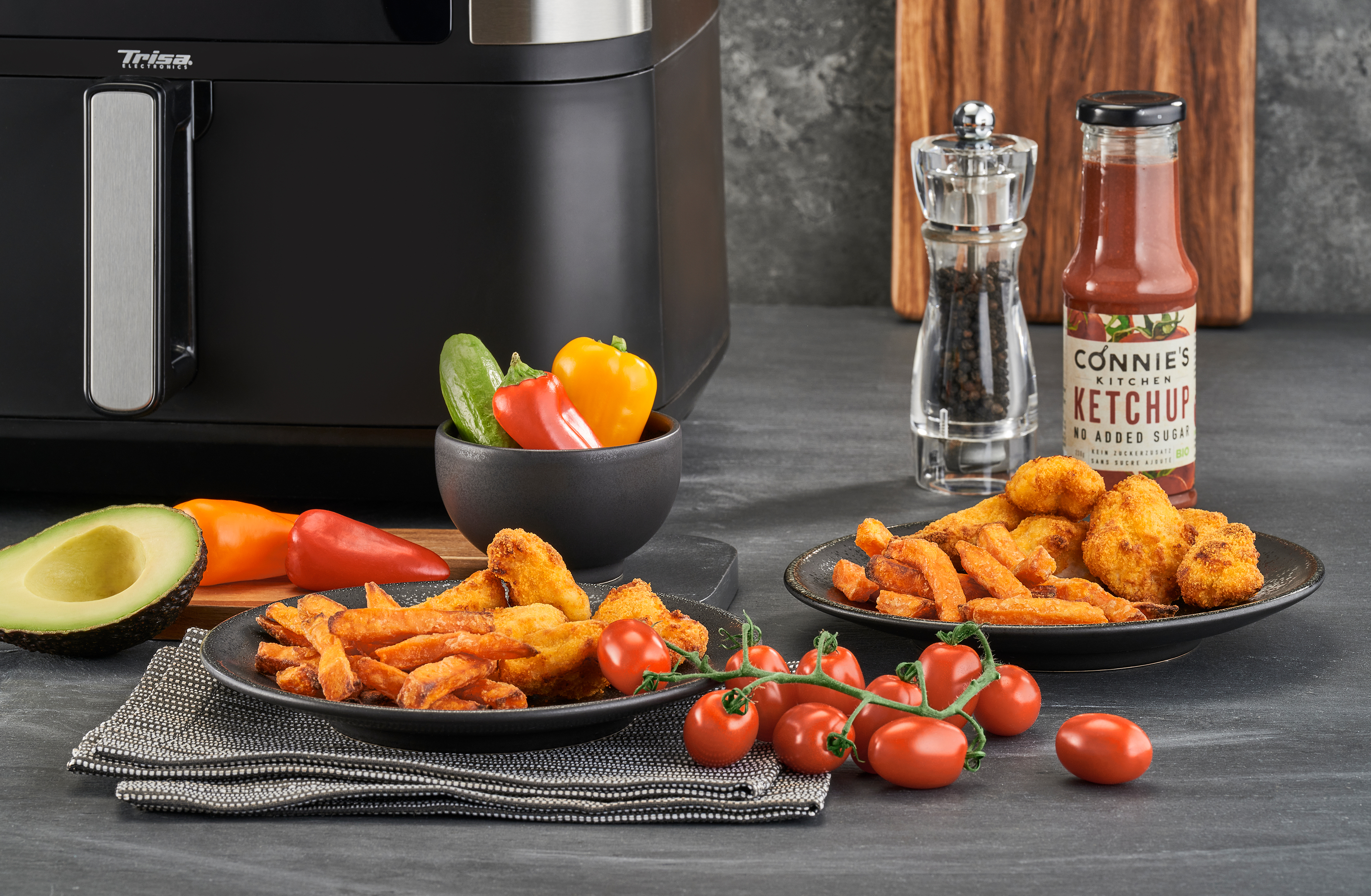 Heißluftfritteuse mit gekochten Pommes, Chicken Nuggets, frischem Gemüse, Ketchup und mehr.