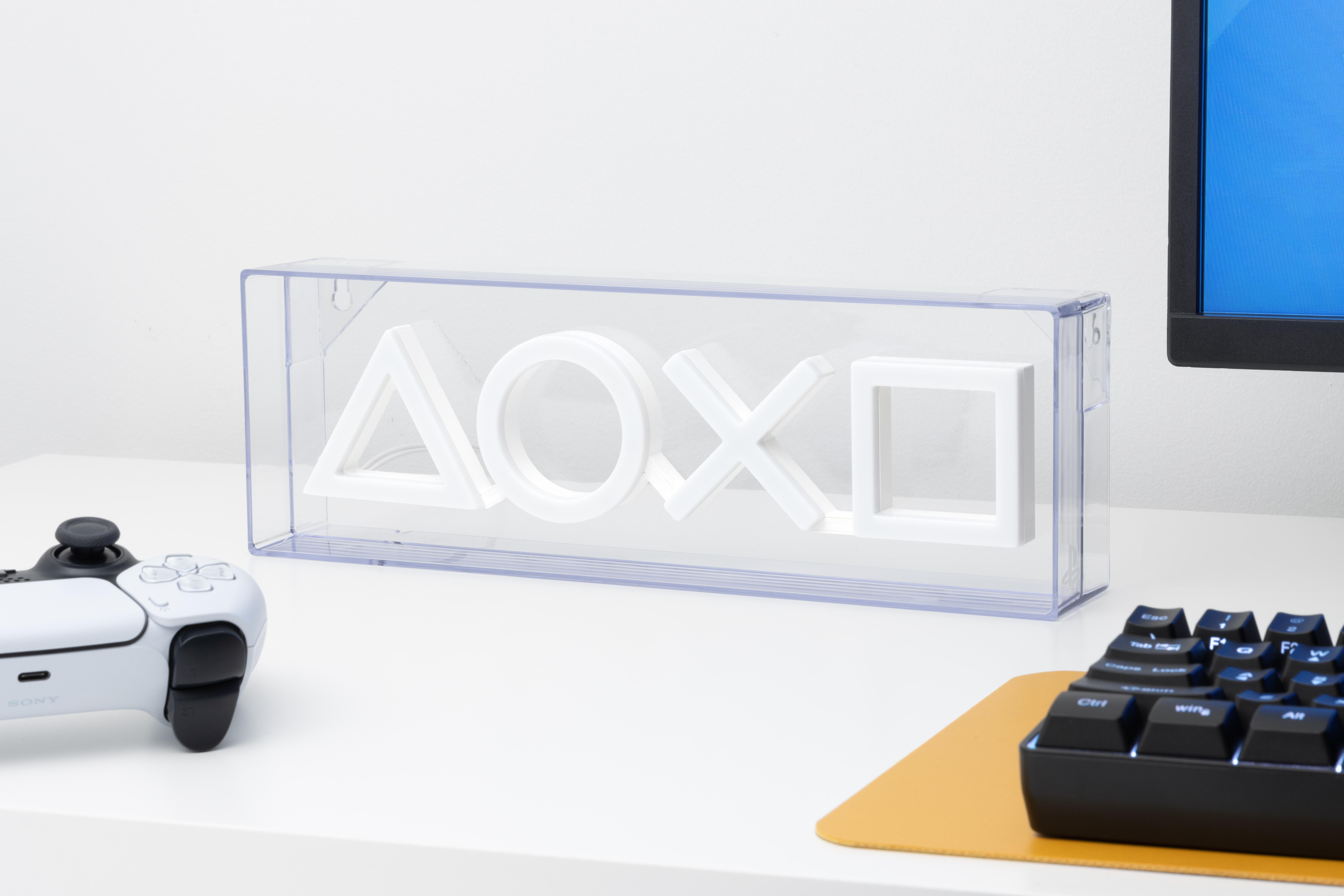 Eine transparente Box mit beleuchteten PlayStation-Symbolen auf einem Schreibtisch, Controller daneben.