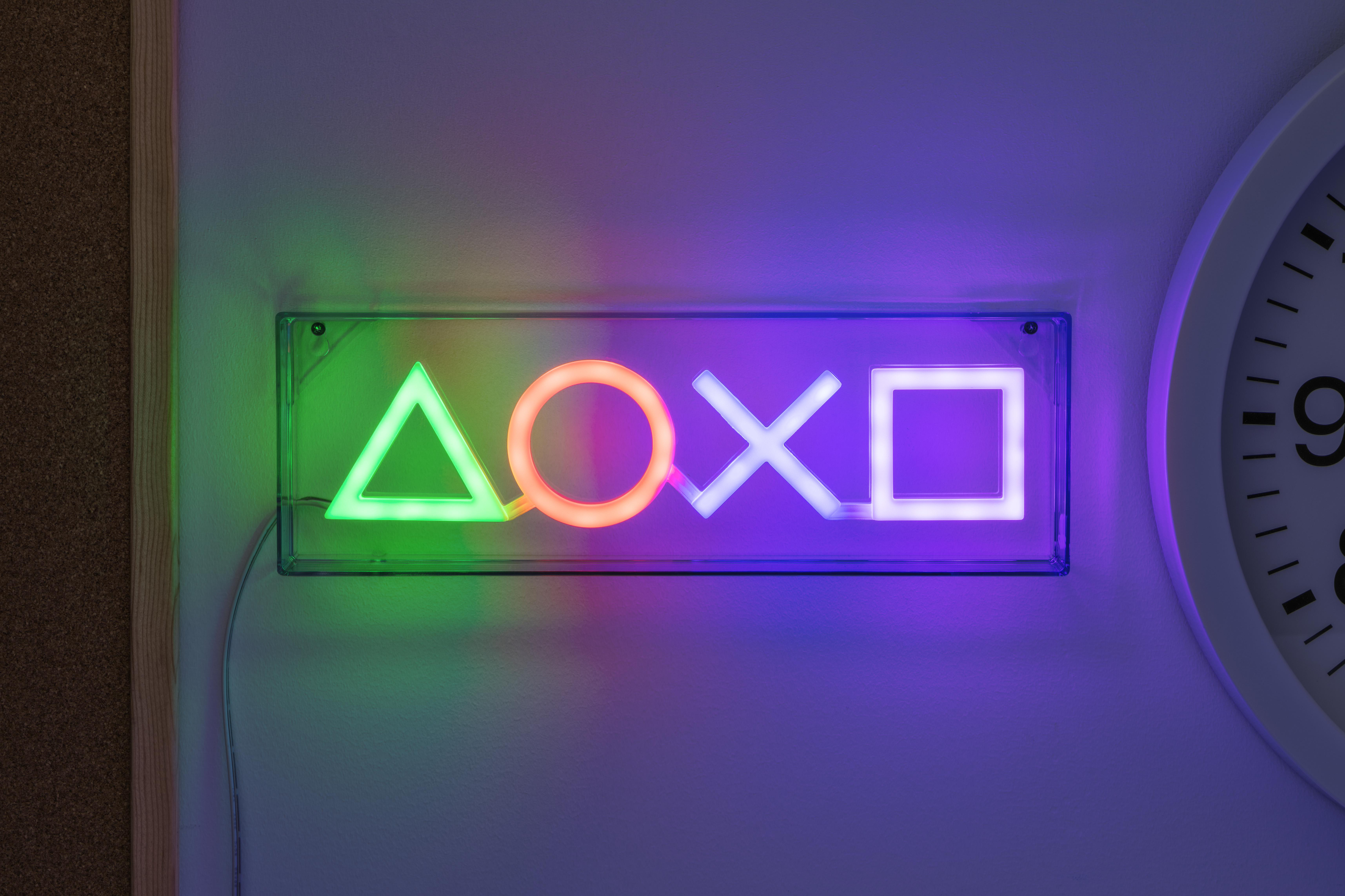 Ein Neonschild mit PlayStation-Symbolen, grün, rot, violett und blau beleuchtet.