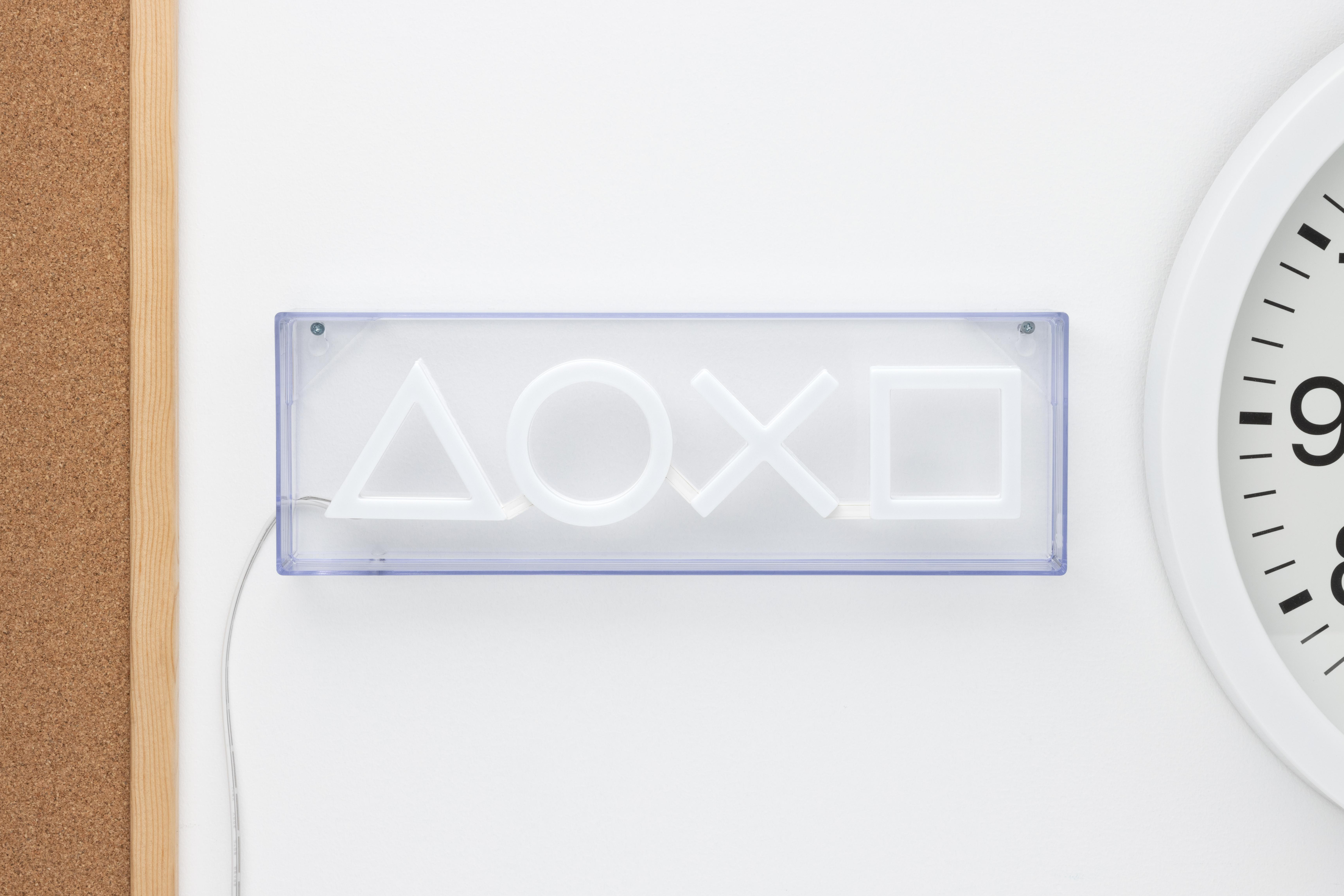 Ein weißes Neon-Schild mit PlayStation-Symbolen an einer weißen Wand.