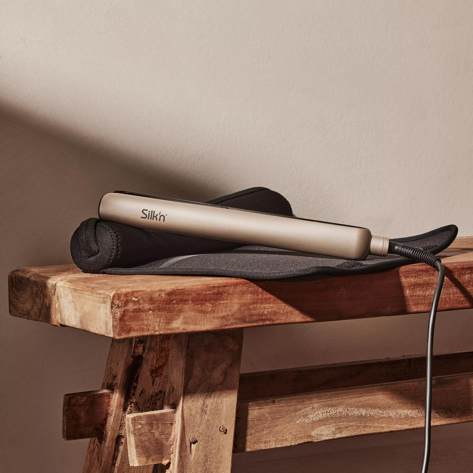 Złota prostownica do włosów na czarnej, żaroodpornej macie na drewnianej ławce.