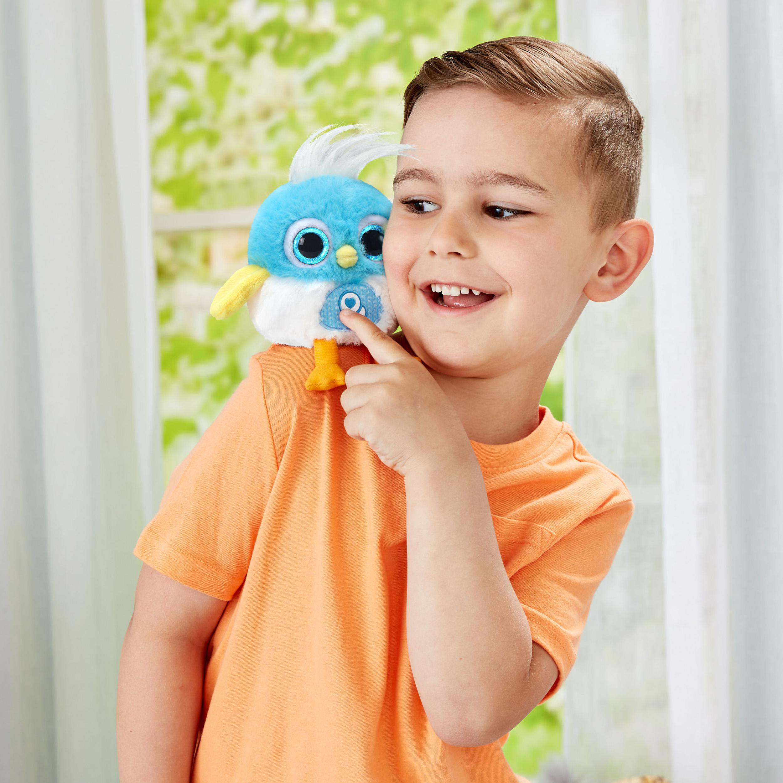 Ein lächelnder Junge zeigt auf ein blaues Vogelspielzeug auf seiner Schulter.