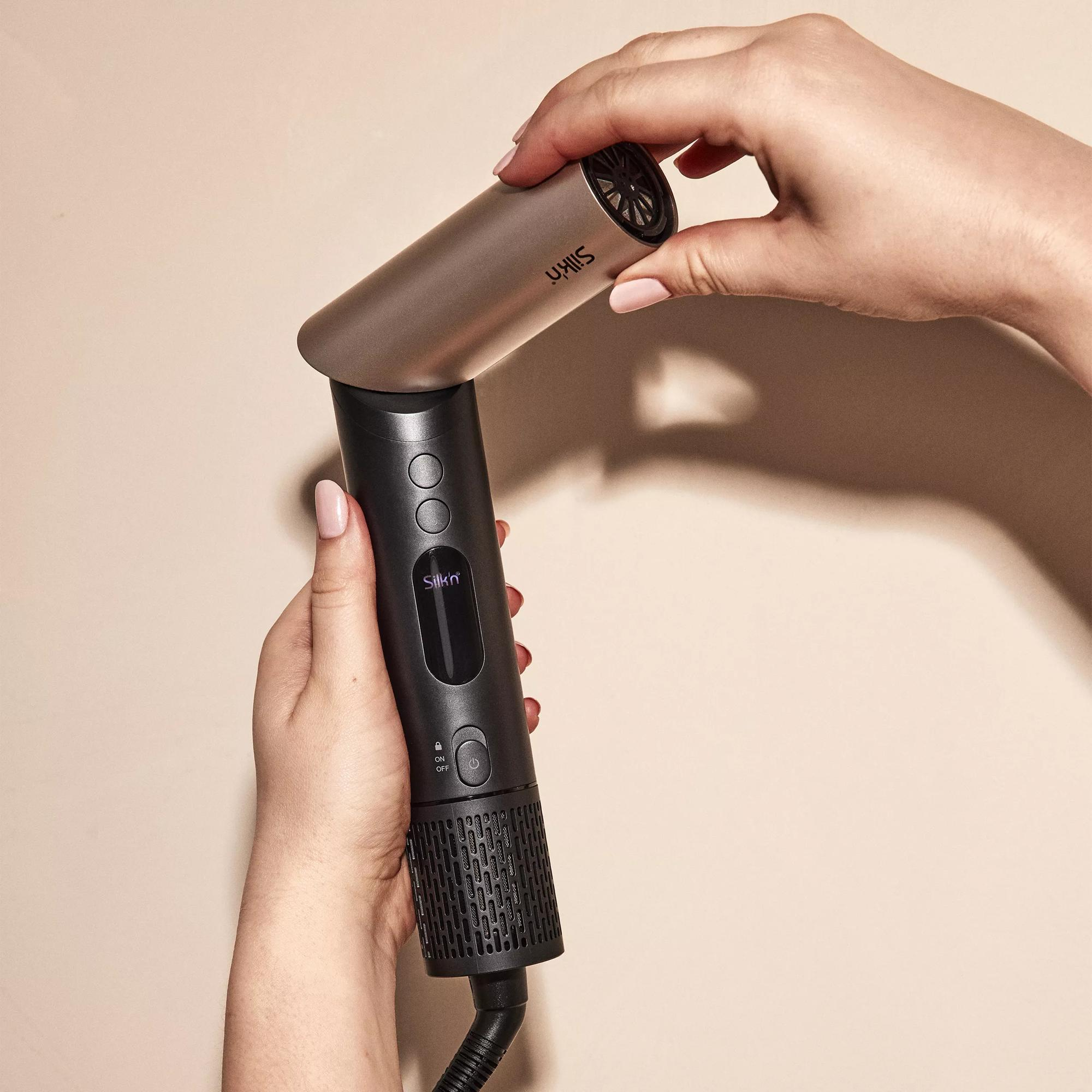 Dłonie trzymające suszarkę do włosów Silkn, kolory czarny i brązowy, neutralne tło.