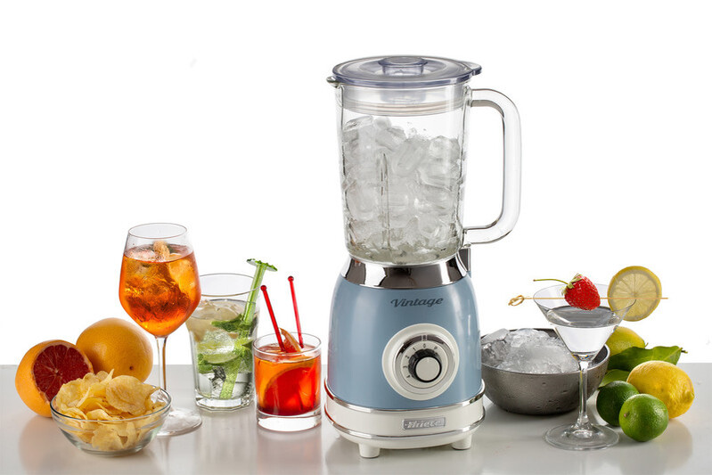 Buzlu, açık mavi bir blender. Kokteyller, meyveler ve cipsler beyaz bir yüzeyde düzenlenmiş.