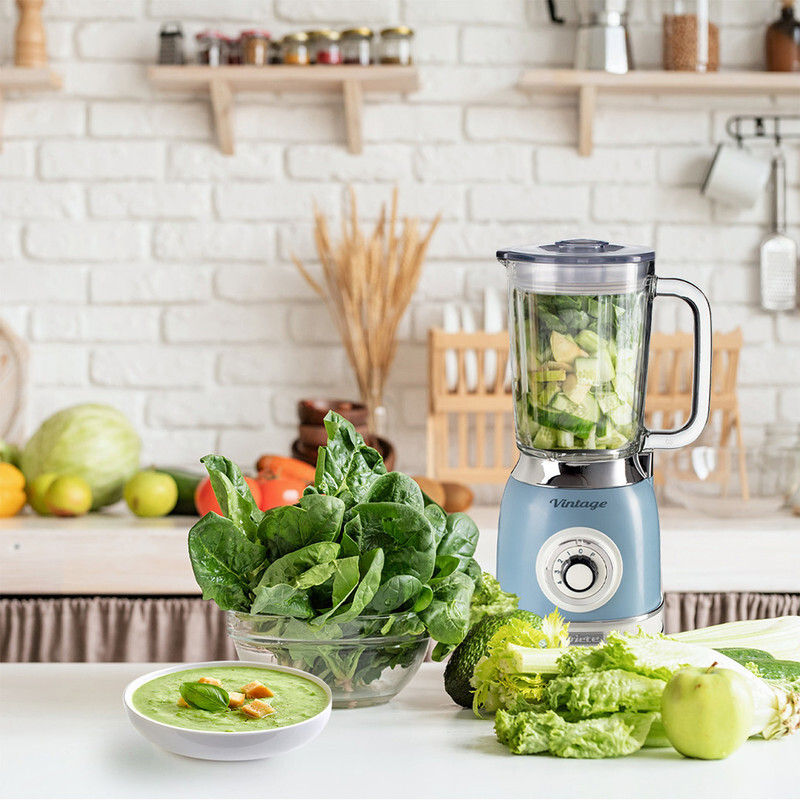 Mutfak sahnesi, mavi bir blender, ıspanak ve diğer sebzeler beyaz bir yüzey üzerinde.