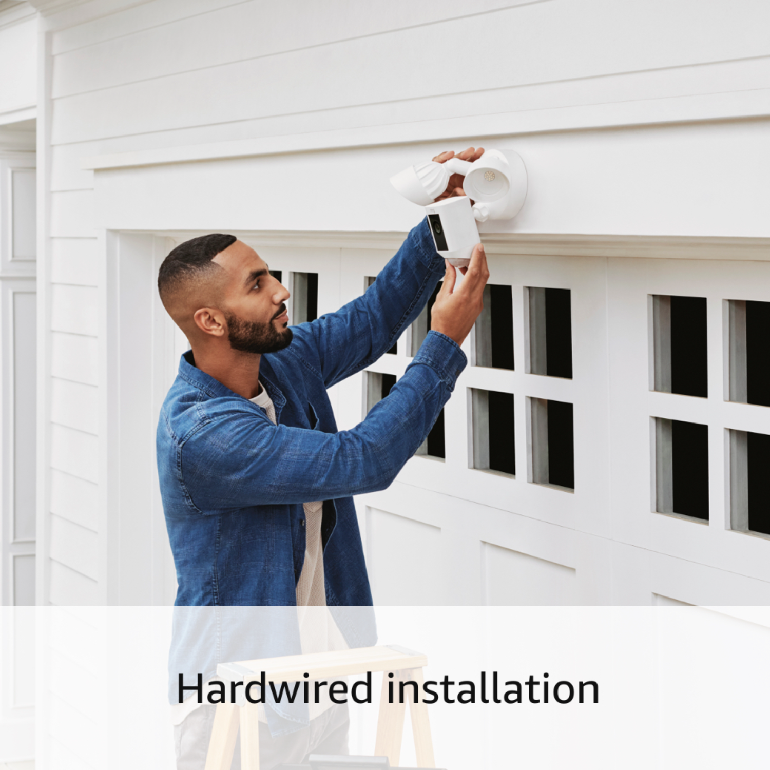 Man installing a white security light fixture on a white exterior wall.
