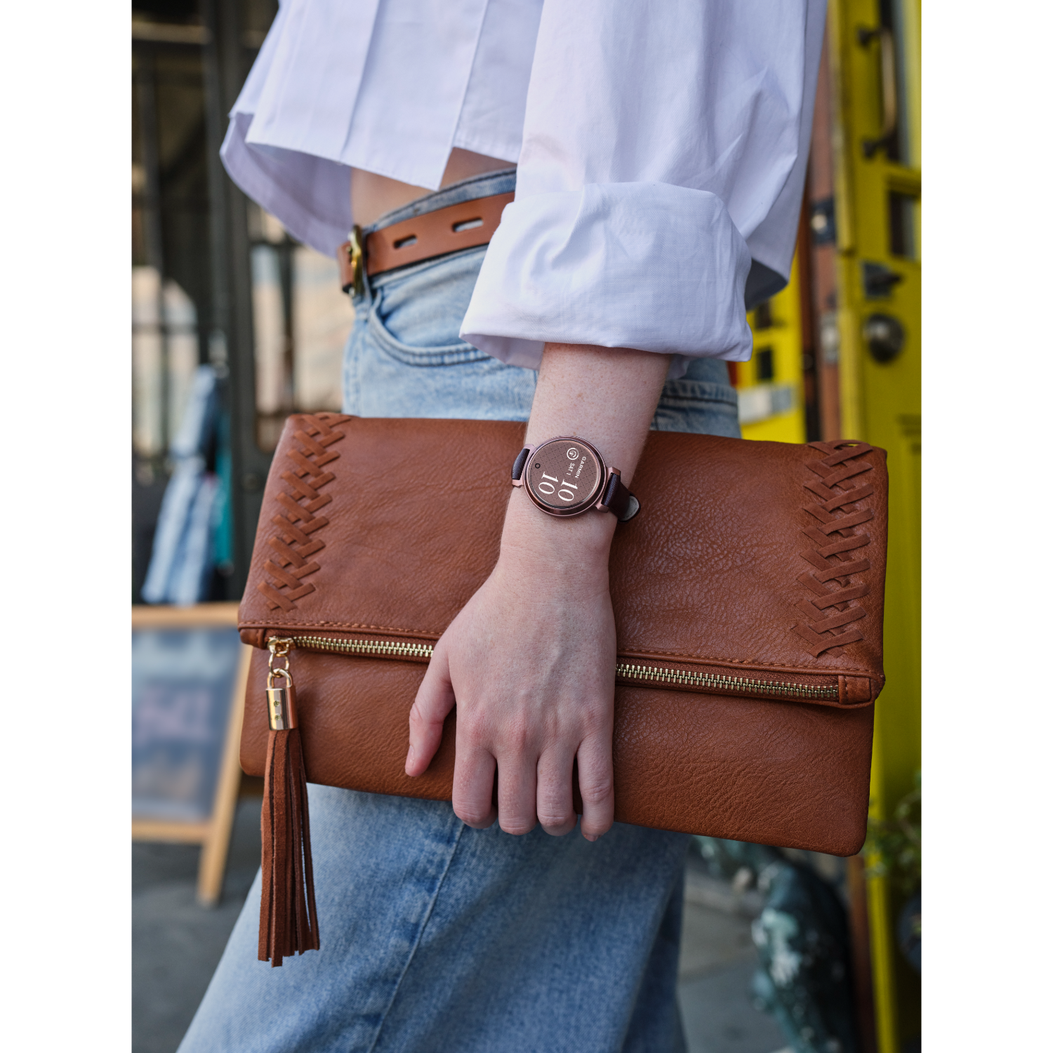 Woman with a brown clutch and a smartwatch, wearing a white shirt and jeans.