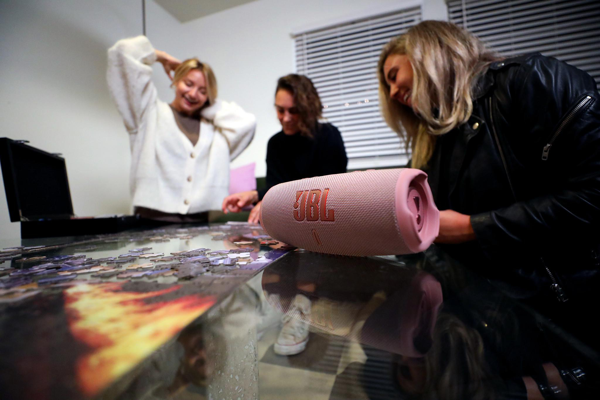 Drei Personen um einen Tisch mit einem Puzzle und einem rosa Lautsprecher.