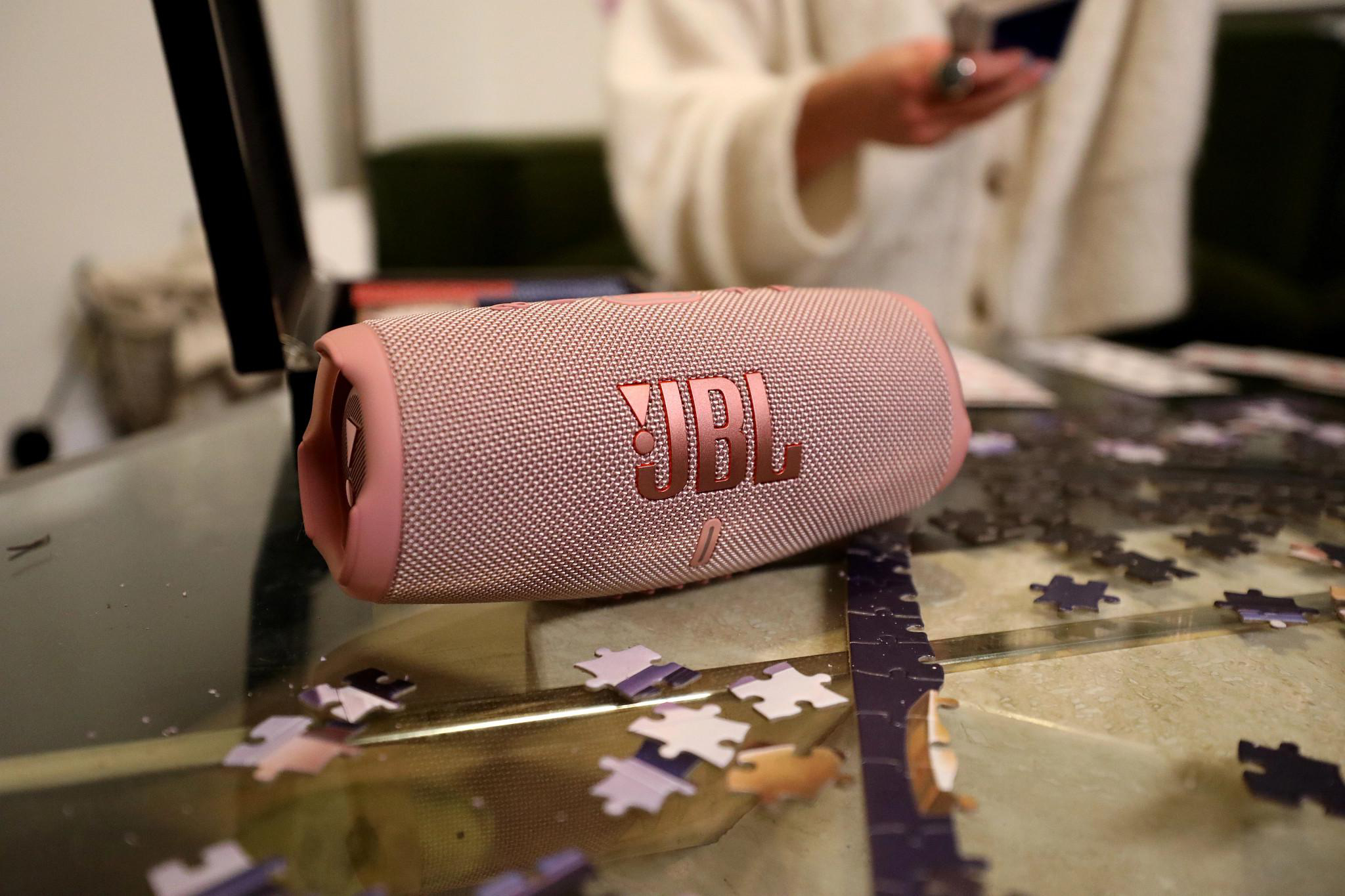 Rosa JBL-Lautsprecher auf einem Tisch mit Puzzleteilen in der Nähe.