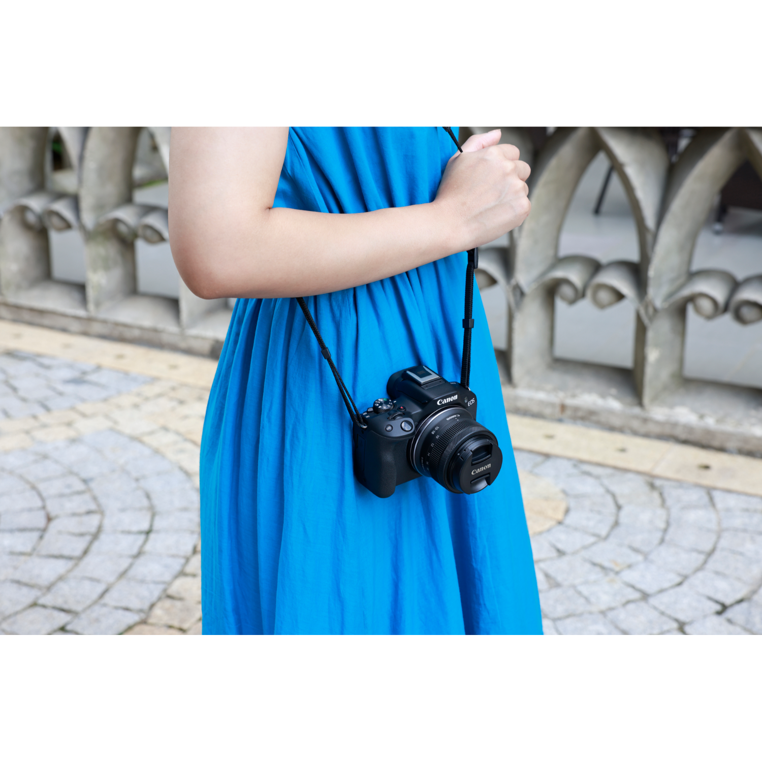 A woman in a blue dress, holding a black camera with a strap around her neck.