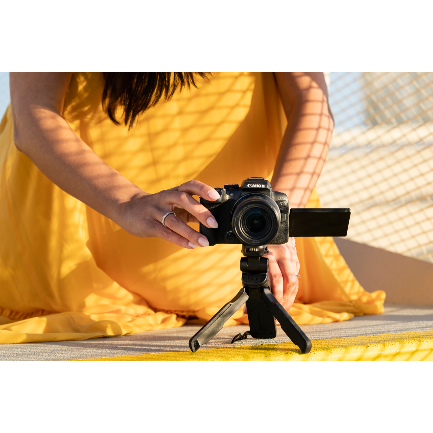 Woman holding a camera on a tripod, wearing a yellow dress.