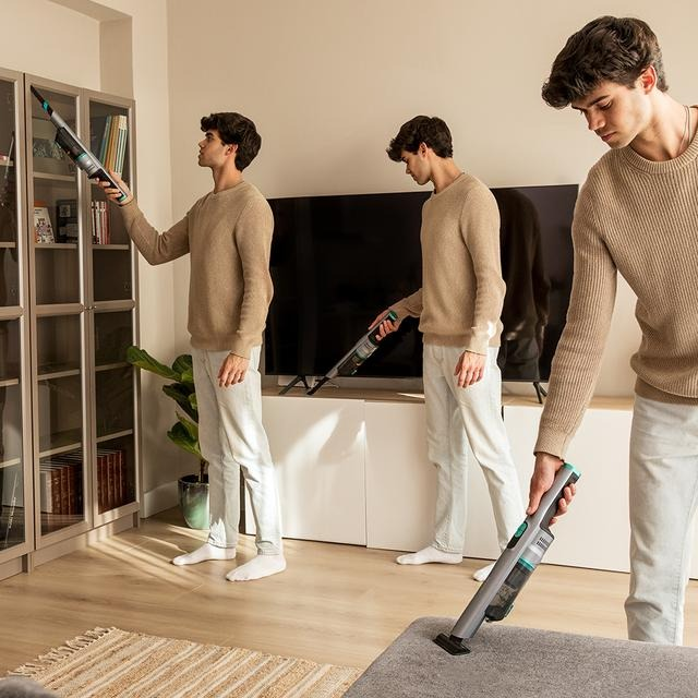 Tres hombres limpiando con una aspiradora inalámbrica en una sala de estar. Muebles al fondo.