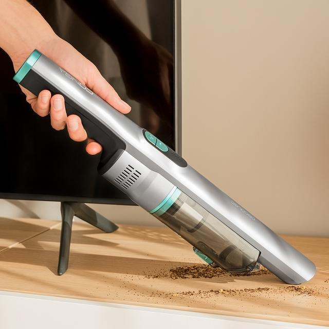 Mano sosteniendo una aspiradora plateada y gris, limpiando una superficie de madera.